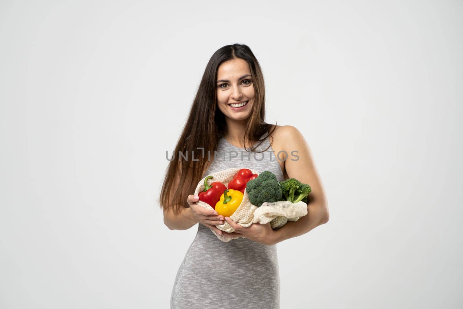Smiling brunette girl is holding mesh shopping bag with vegetables, greens without plastic bags. Zero waste, plastic free Eco friendly concept. Sustainable lifestyle. by vovsht