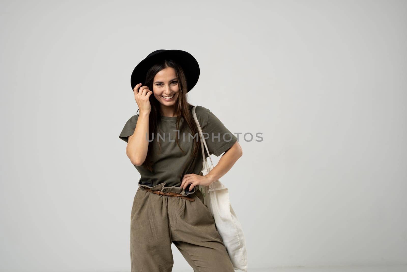 Happy smiling brunette woman in black hat with white cotton eco bag on her shoulder. Girl holding textile grocery bag with vegetables. Zero waste concept