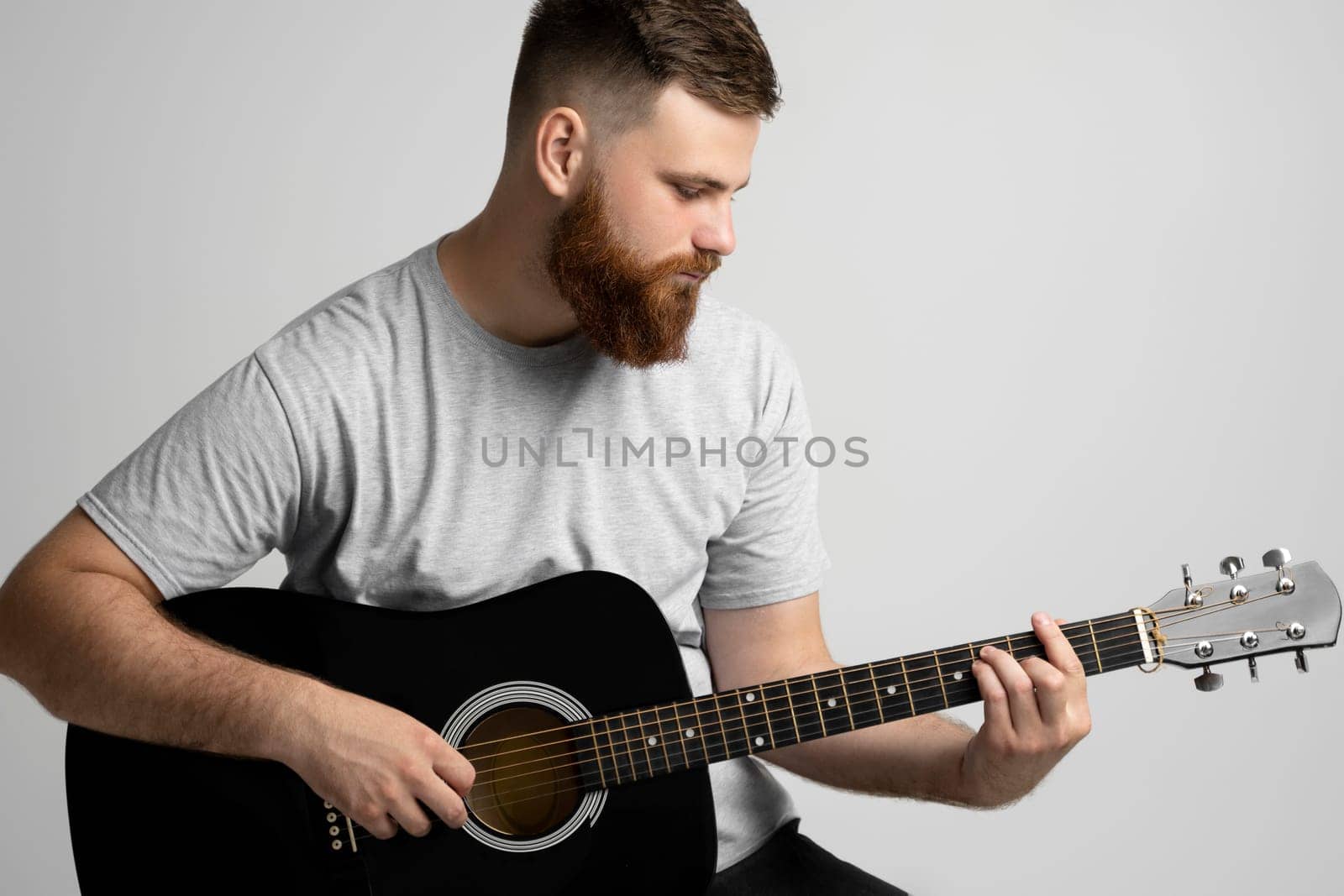 A young stylish men with a beard with a acoustic guitar on a white background. Music performer musician. Musical string instrument