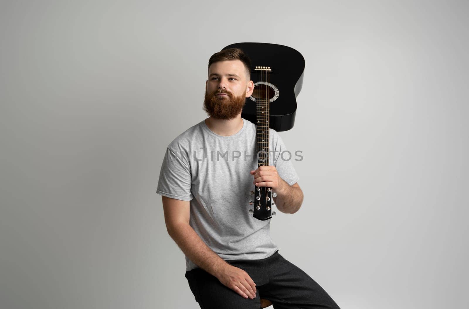 Bearded man in grey t-shirt with a acoustic guitare. Music performer musician. Mature charismatic male guitarist with a string instrument. by vovsht