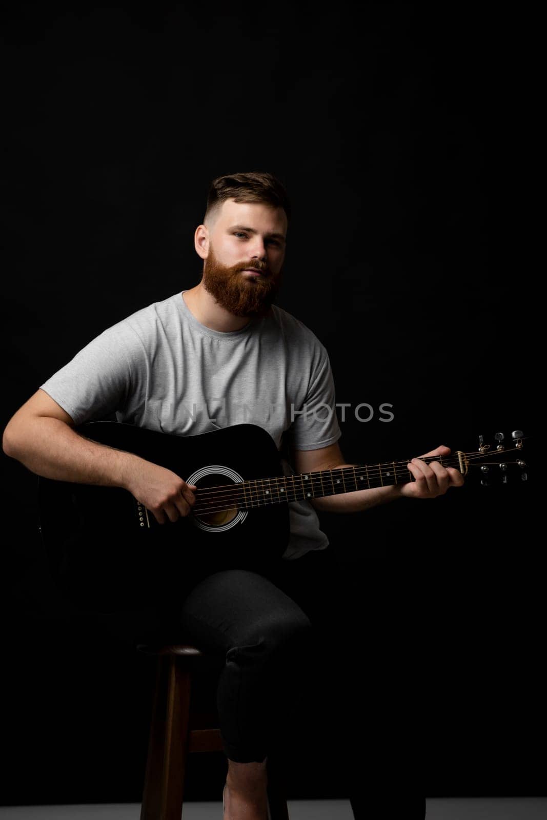 Portaraite of bearded musician man playing acoustic guitar in a dark room. by vovsht