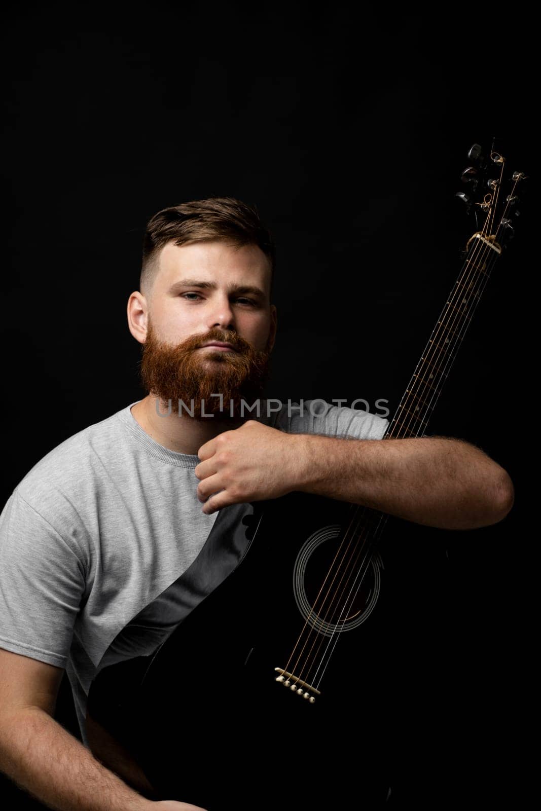 Portraite of bearded handsome musician holding a guitar in a dark room. Guitarist, artist, composer, rocker, star. by vovsht