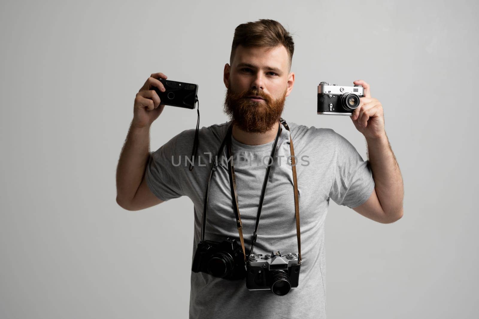 Professional bearded photographer holding a bunch of different vintage old cameras in a hands and on a shoulder. by vovsht