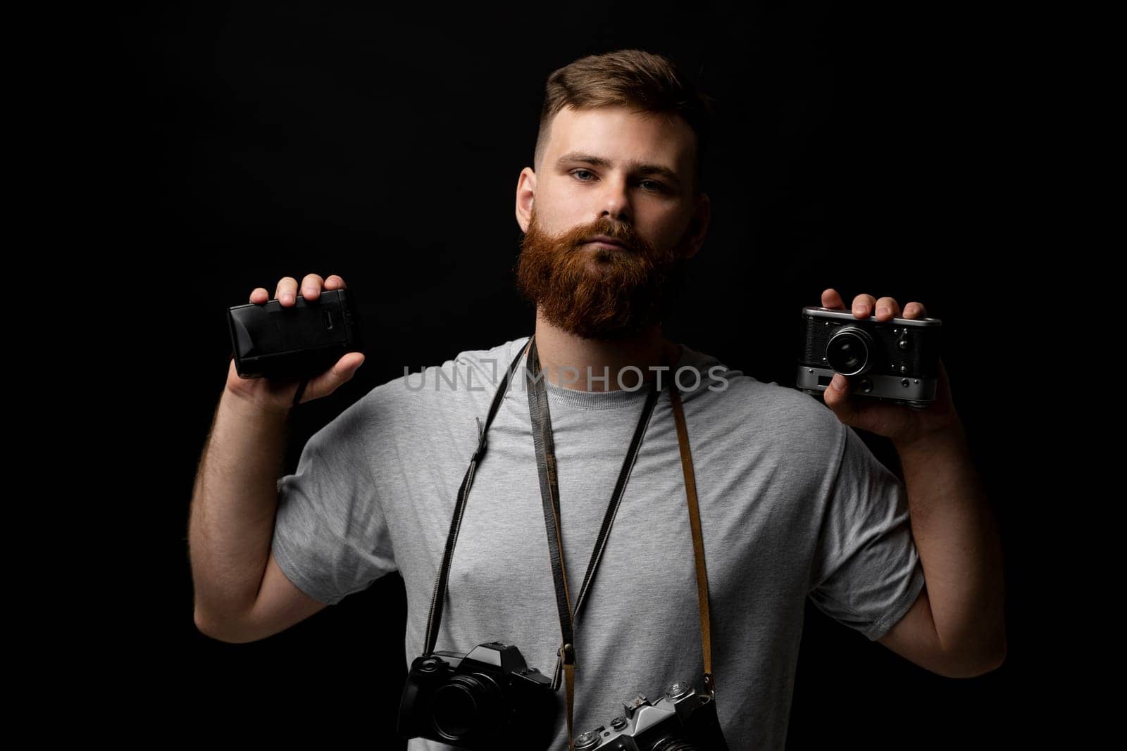 Professional bearded photographer holding a bunch of different vintage old cameras in a hands and on a shoulder. by vovsht