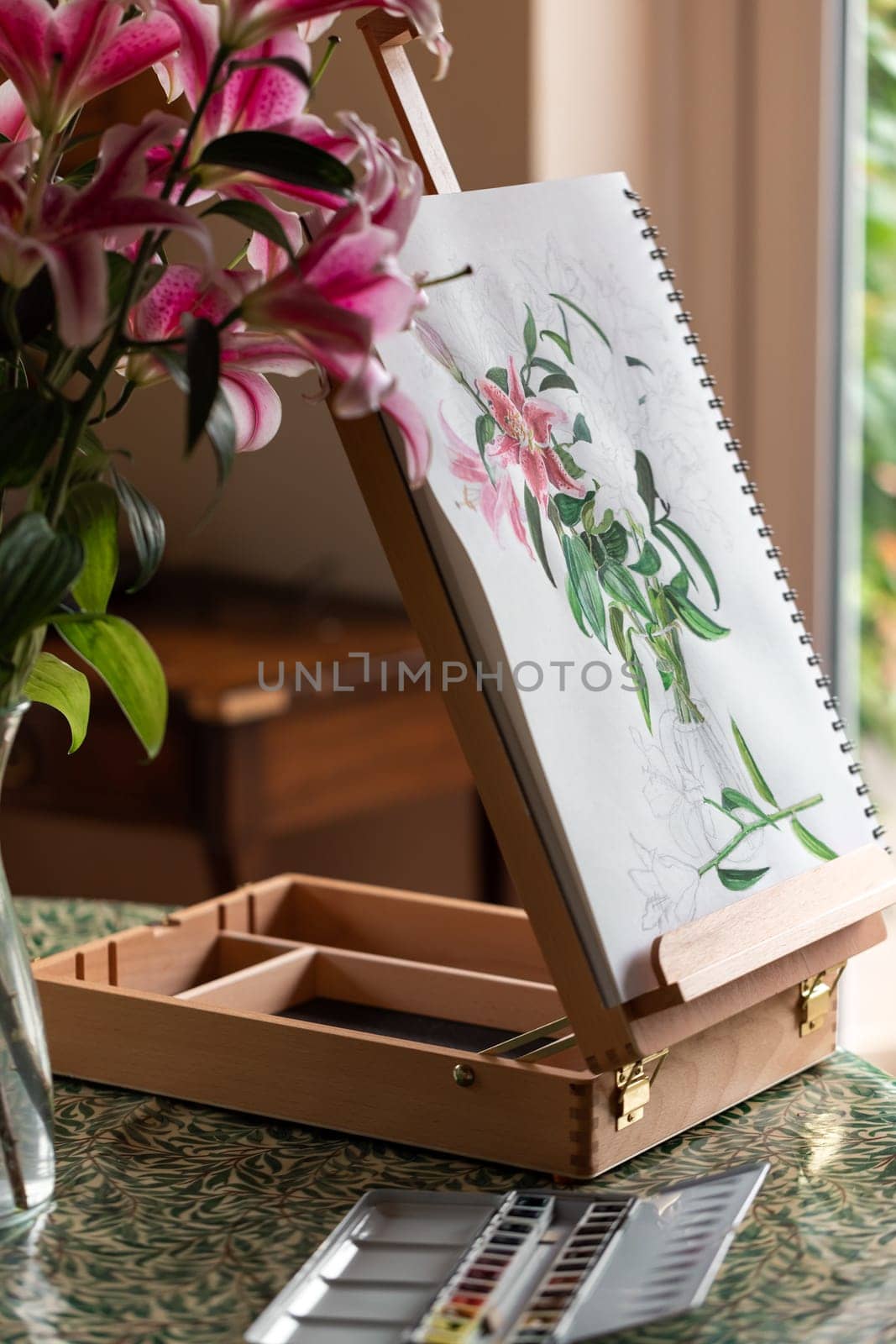The easel with still life with purple lilies watercolor on the table prepared for painting at home