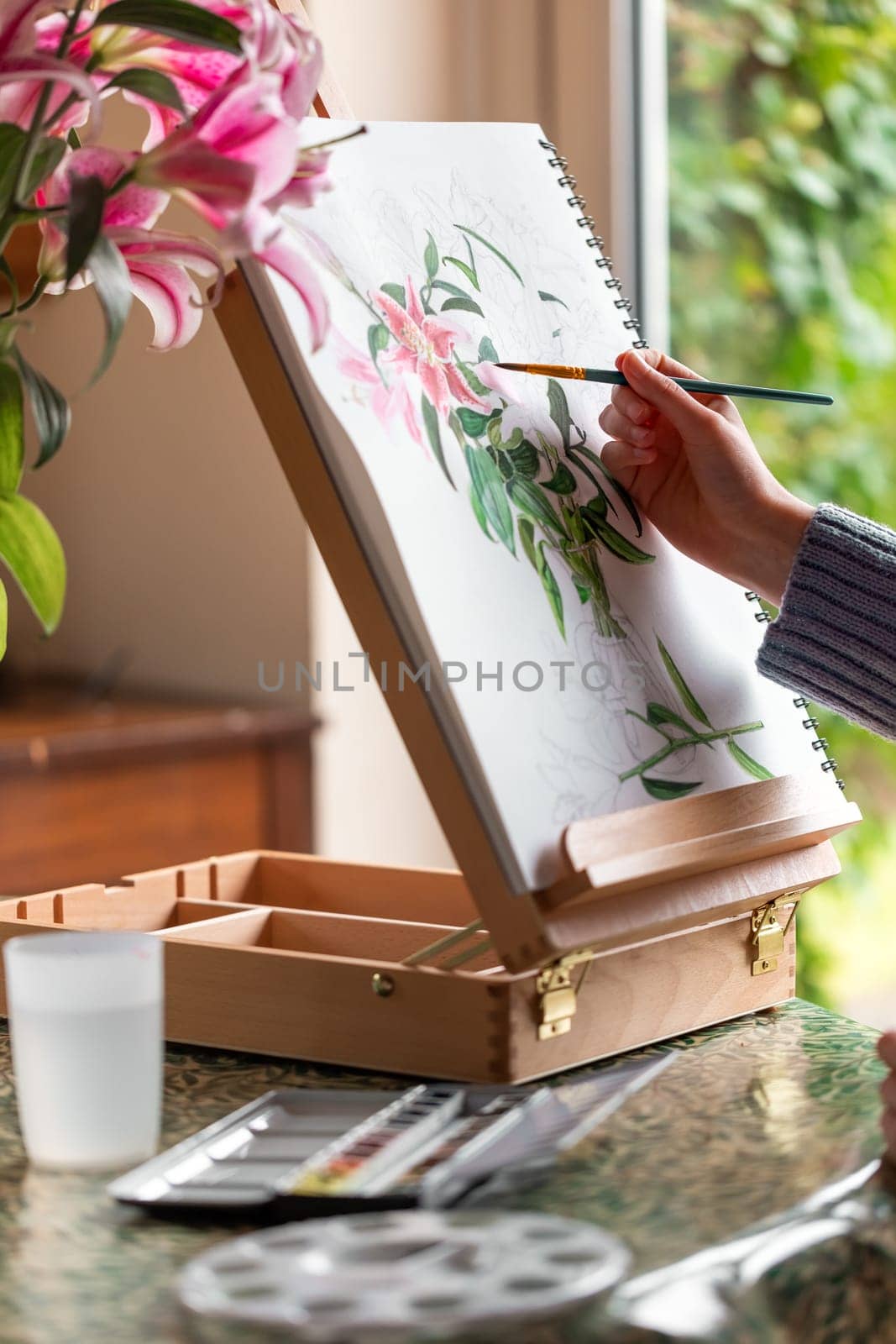 Young girl painting still life with flowers, purple lilies, with watercolor paints on the easel by Len44ik
