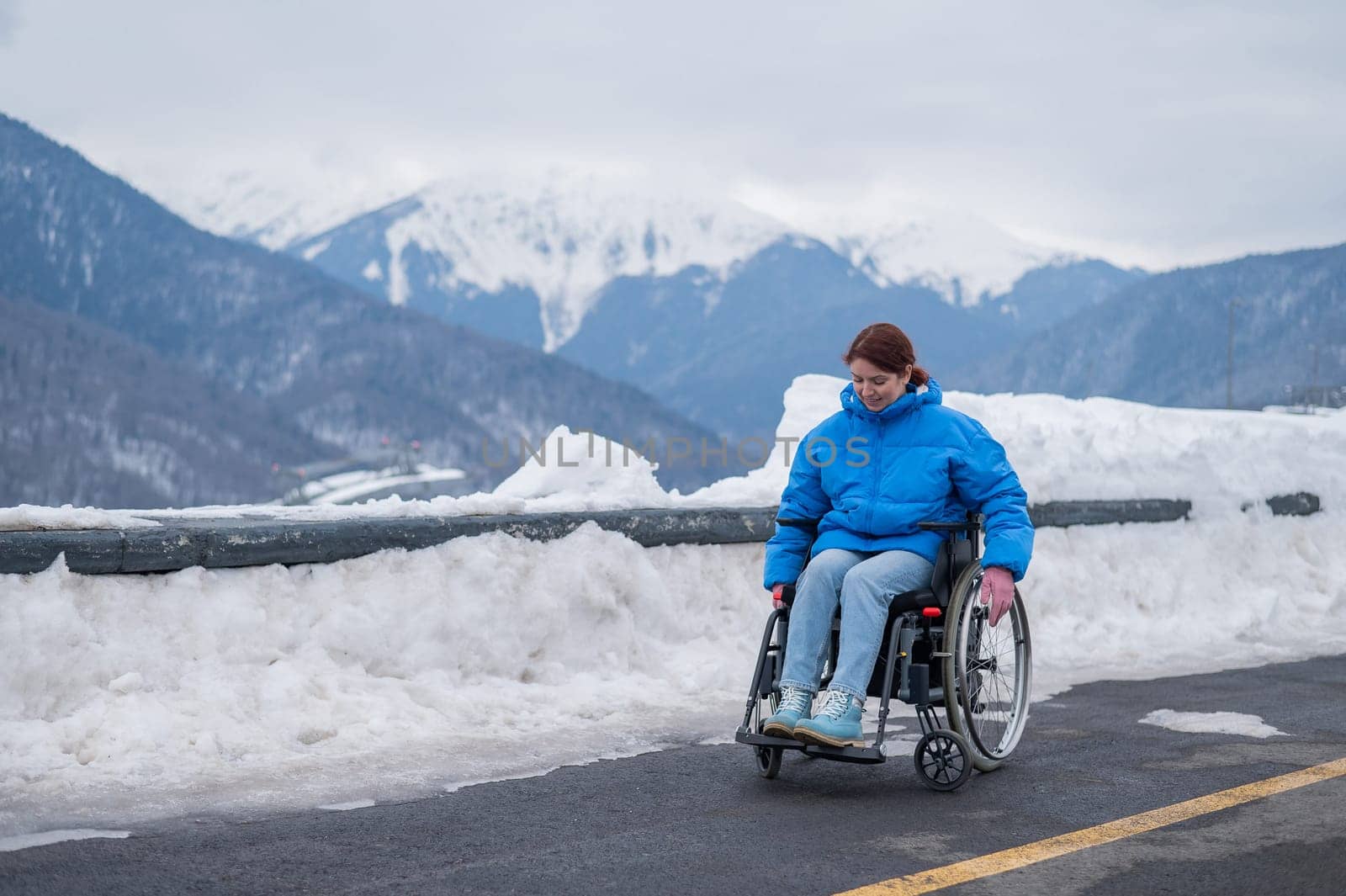 A woman in a wheelchair on a point view admires the high mountains. Thrust to life