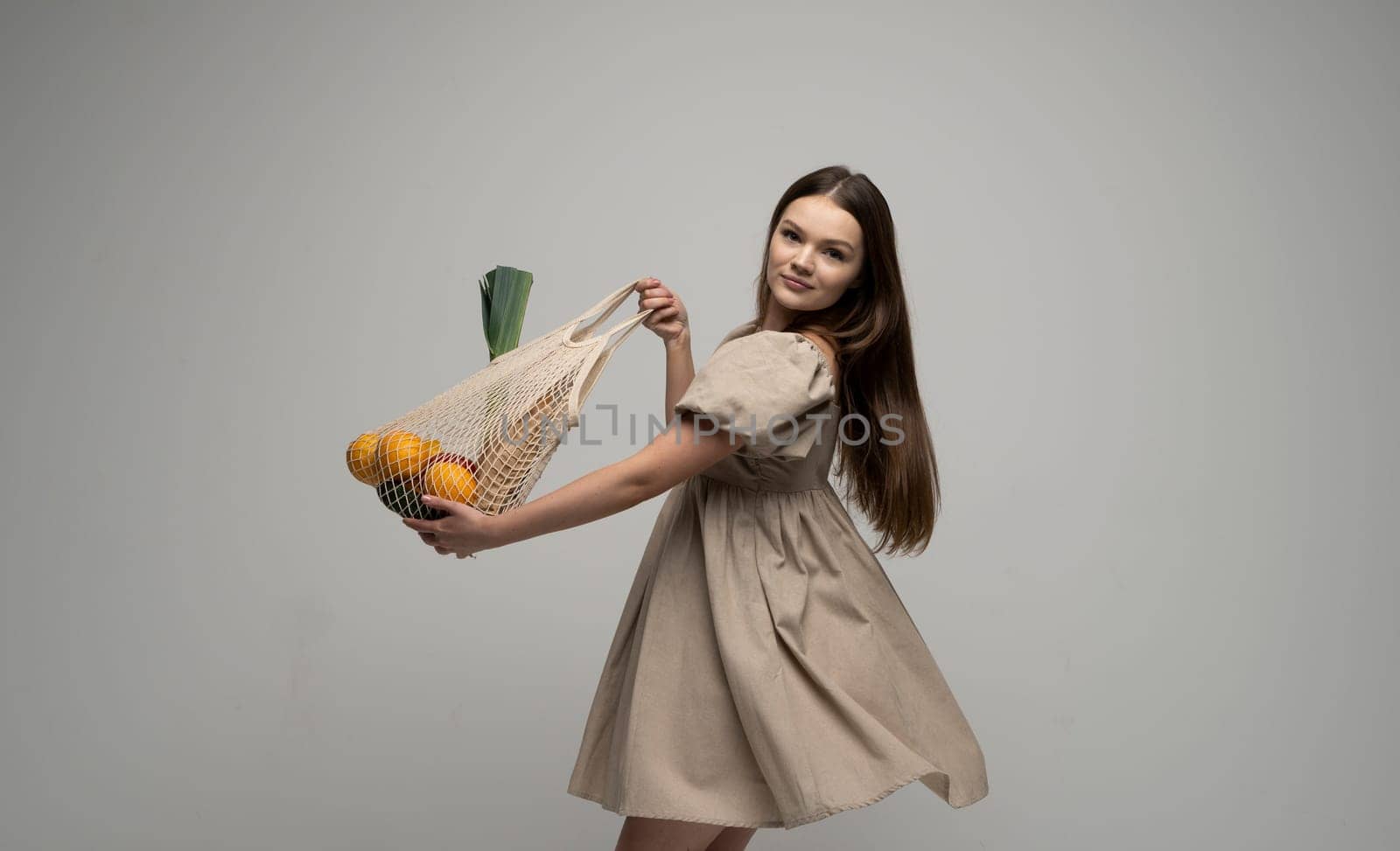 Young woman in a summer dress holding reusable cotton shopping mesh bag with groceries from a market. Concept of no plastic. Zero waste, plastic free. Eco friendly concept. Sustainable lifestyle