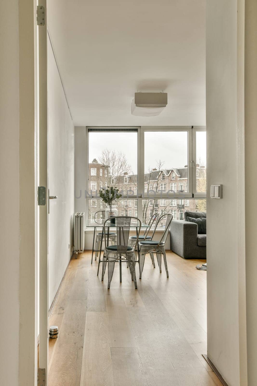 a living room and dining area in an apartment with wood floors, white walls and large windows looking out onto the street