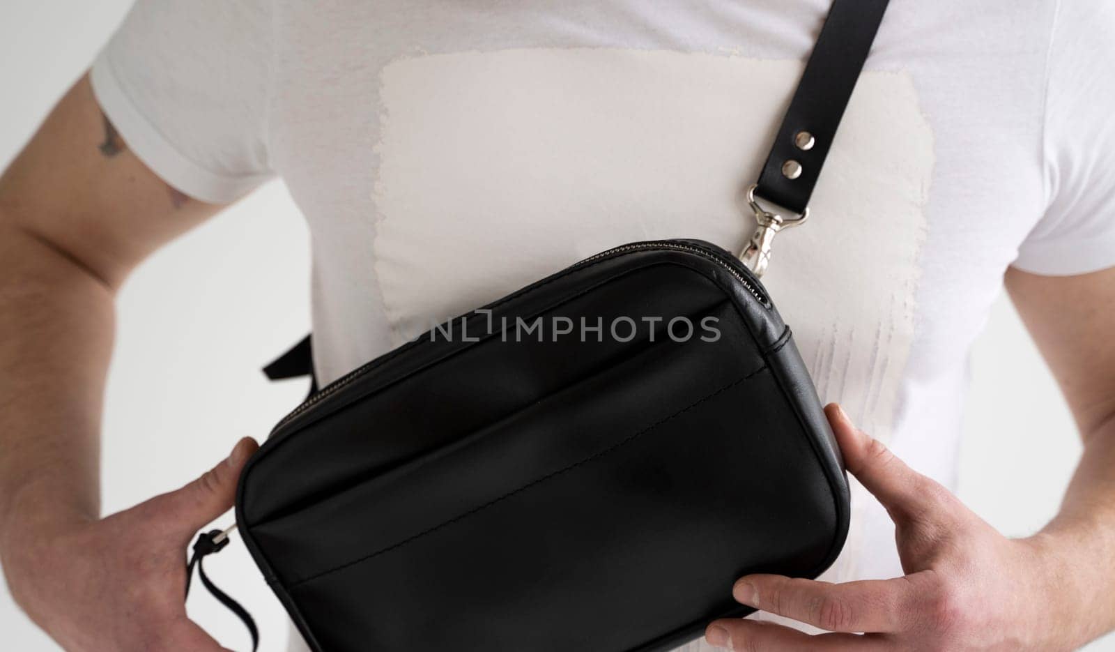 Side view man in a white t-shirt with a leather black handmade bag over his shoulder. Dark designer banana bag. Comfortable small bag for walking