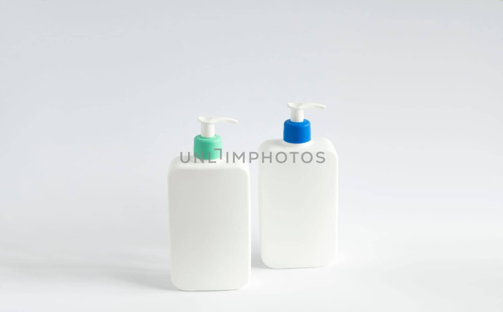 Two white unbranded dispenser bottles on white background. Cosmetic packaging mockup with copy space