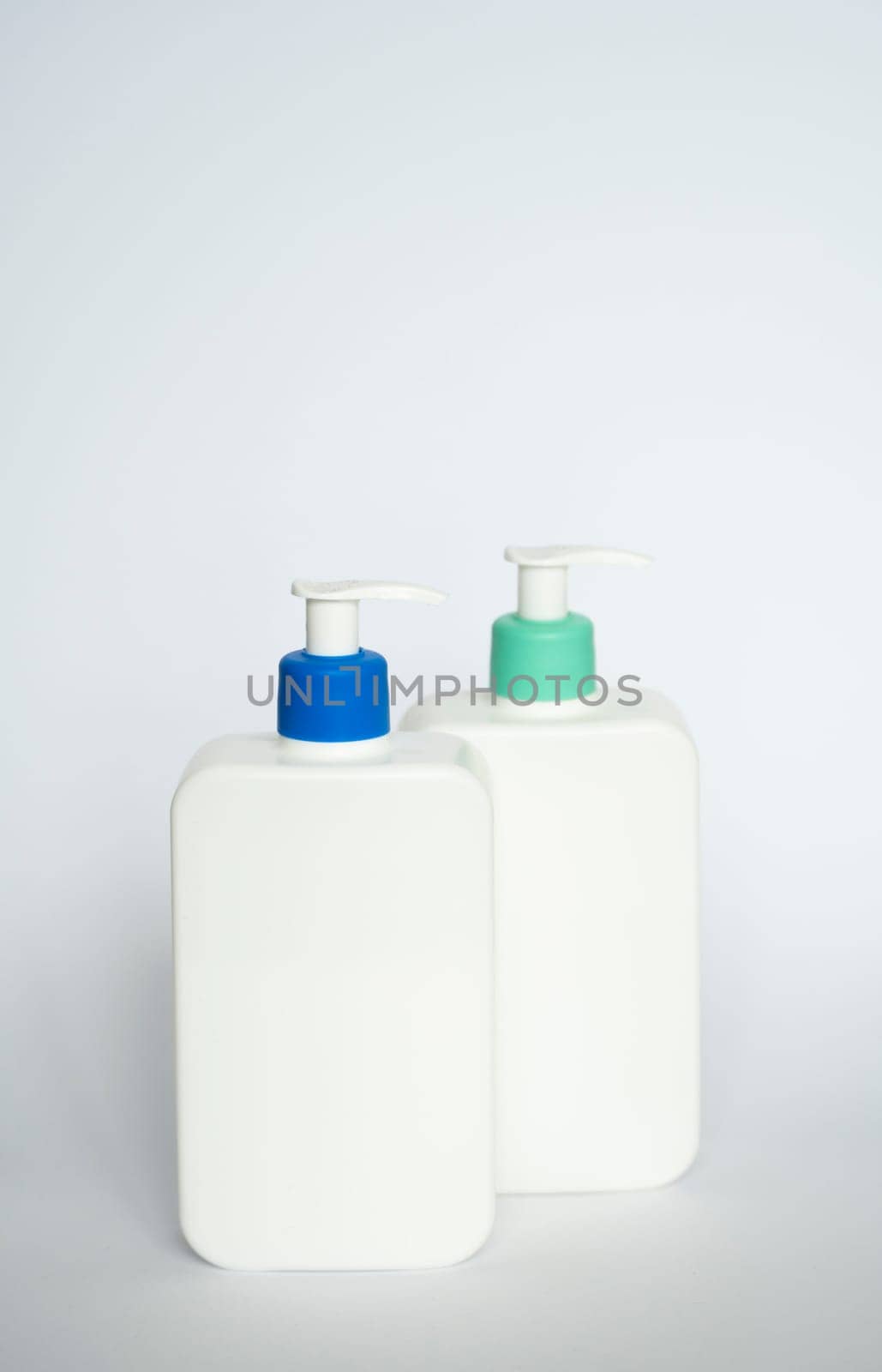 Two white cosmetic plastic bottle with pump dispenser pump and blue cap on white background. Liquid container for gel, lotion, cream, shampoo, bath foam