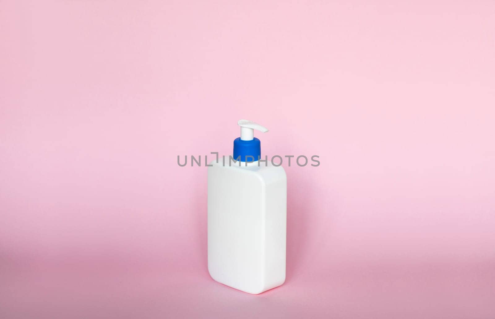 White unbranded bottle with a dispenser isolated on pink background. cosmetic packaging mockup with copy space. Bottle for a shower, gel, soap