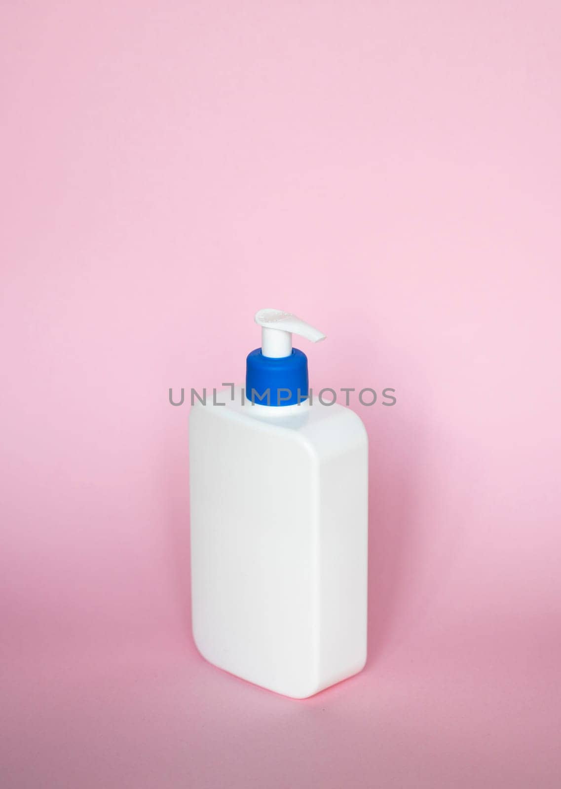 Blank unbranded cosmetic plastic bottle with blue dispenser pump on pink background. White liquid container for shampoo, gel, lotion, cream, bath foam on pink background. by vovsht