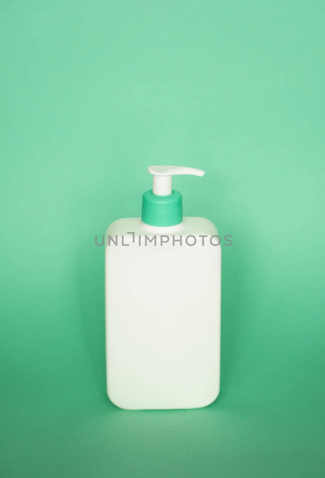 White blank unbranded cosmetic plastic bottle with dispenser pump on green background. Liquid container for shampoo, gel, lotion, cream, bath foam on pink background