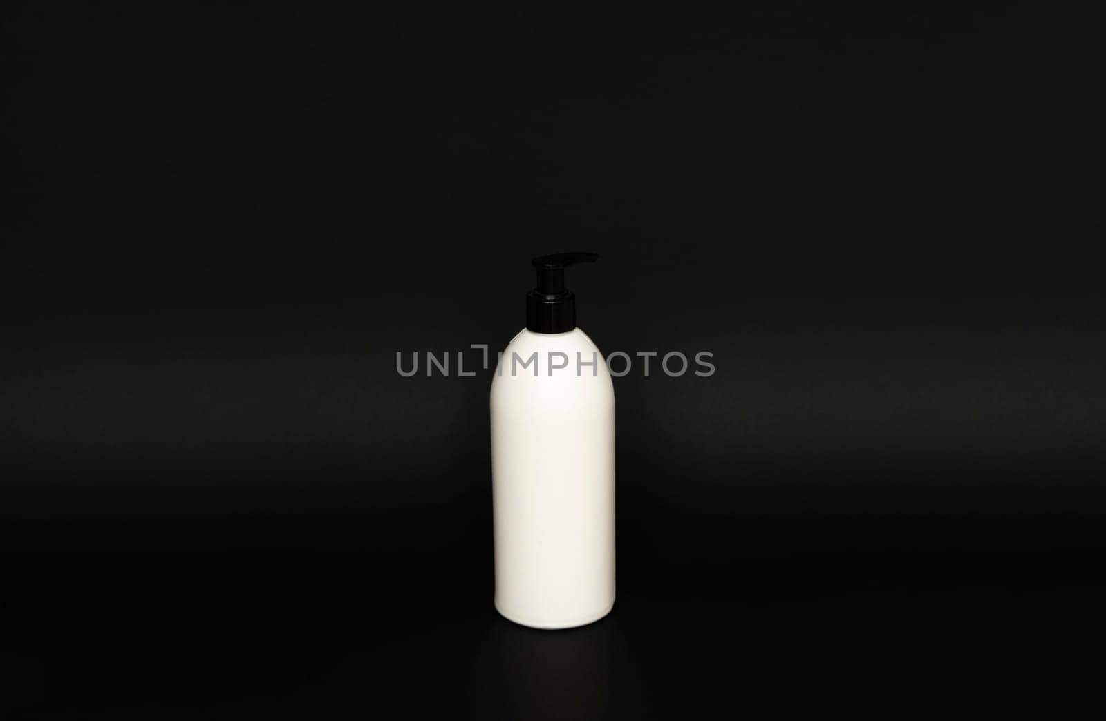 White unbranded bottle with a black dispenser isolated on black background. cosmetic packaging mockup with copy space. Bottle for a shower, gel, soap