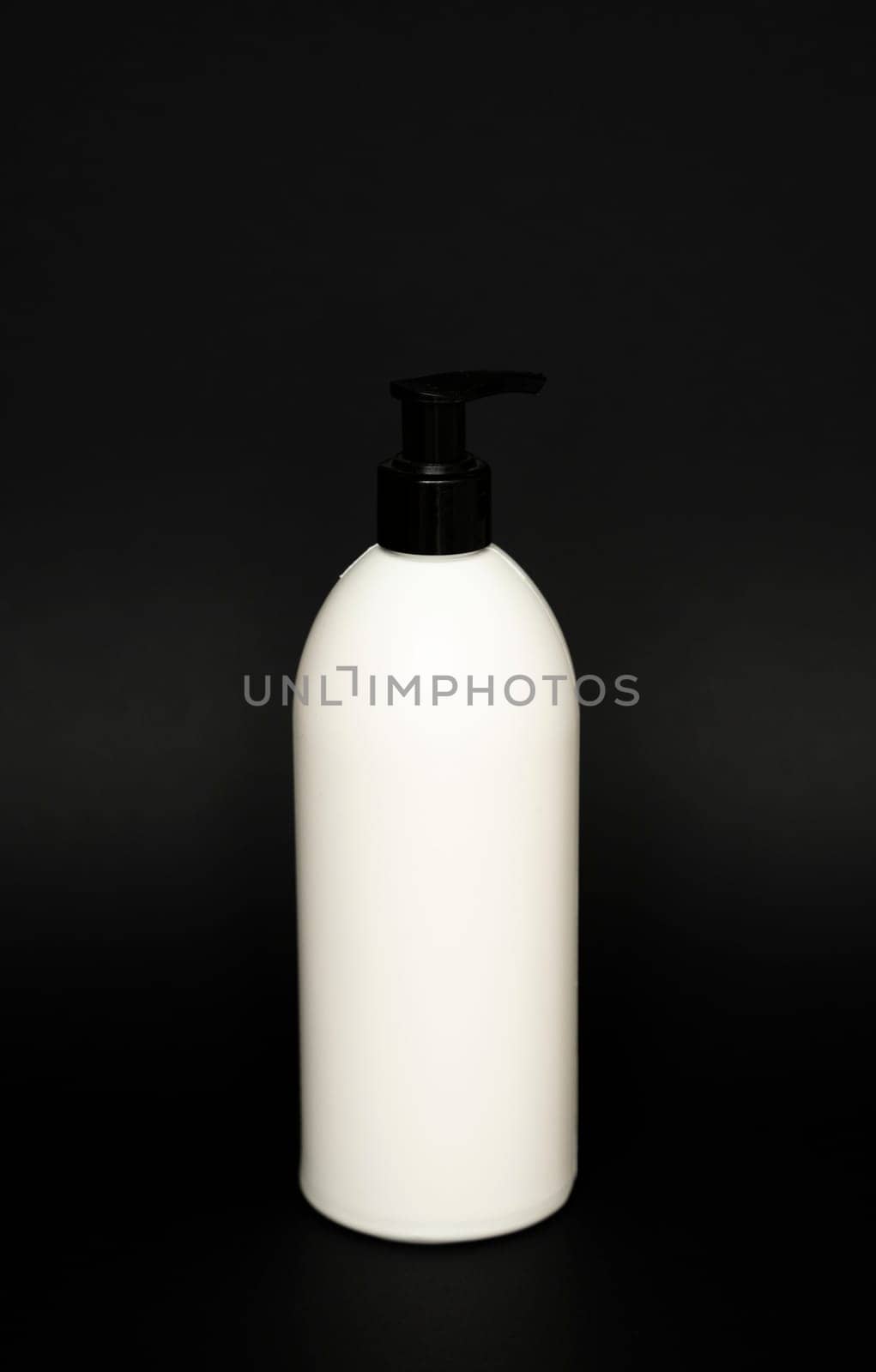 White unbranded bottle with a black dispenser isolated on black background. cosmetic packaging mockup with copy space. Bottle for a shower, gel, soap. by vovsht