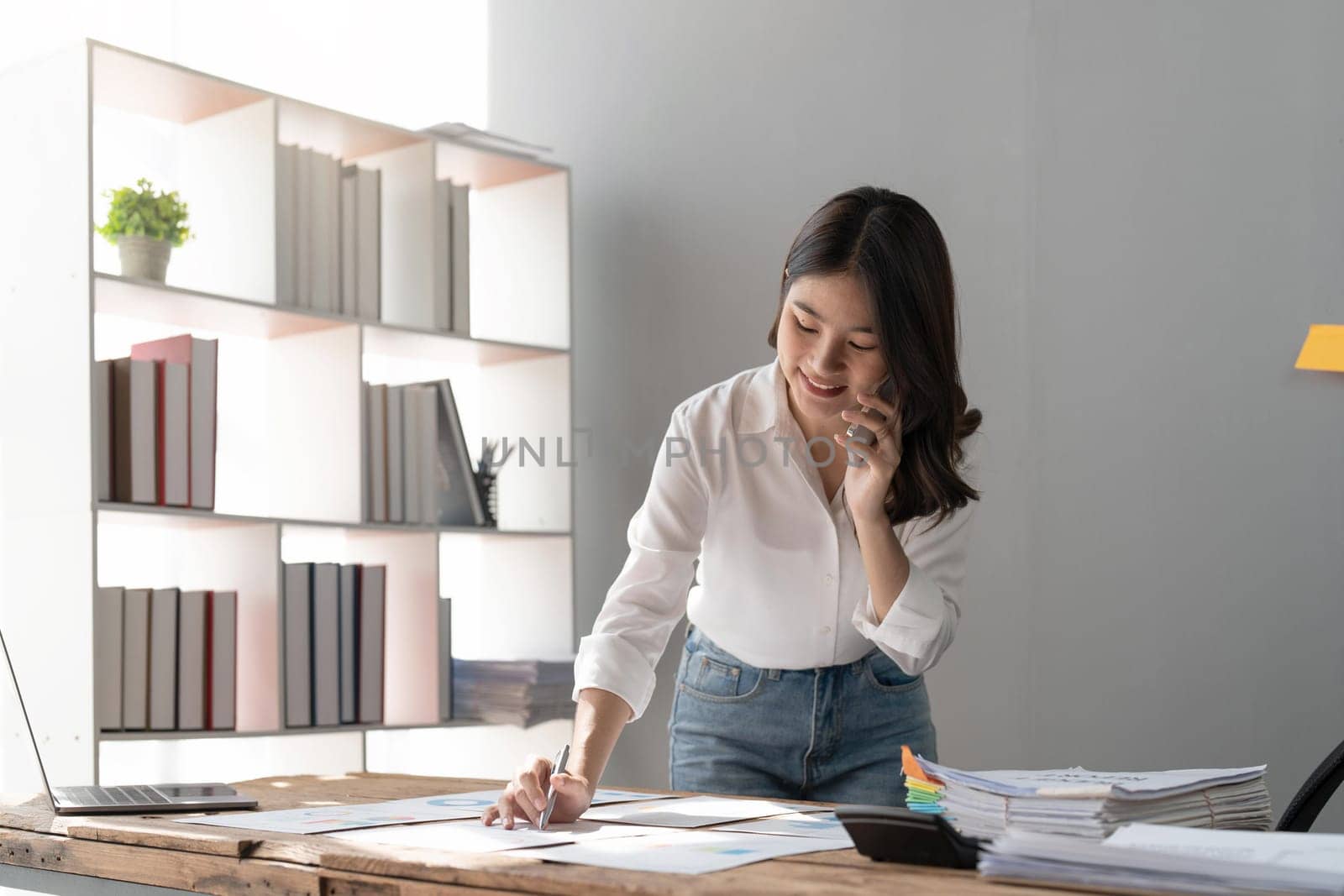 Young businesswoman talking on phone while working project analysis at table in office.