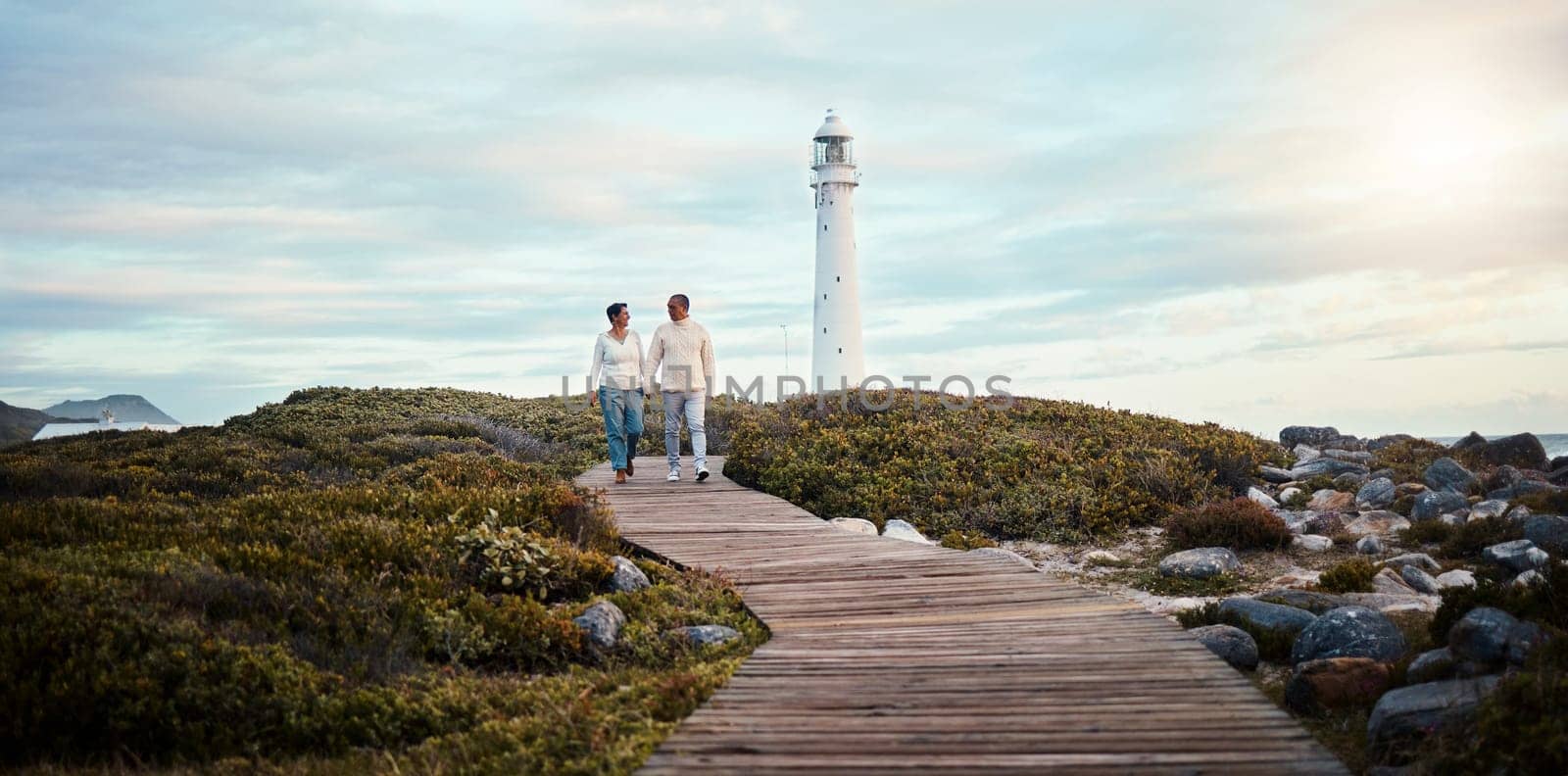 Romance, love and a couple holding hands while walking on the beach with a lighthouse in the background. Nature, view or blue sky mockup with a man and woman taking a romantic walk outside together.
