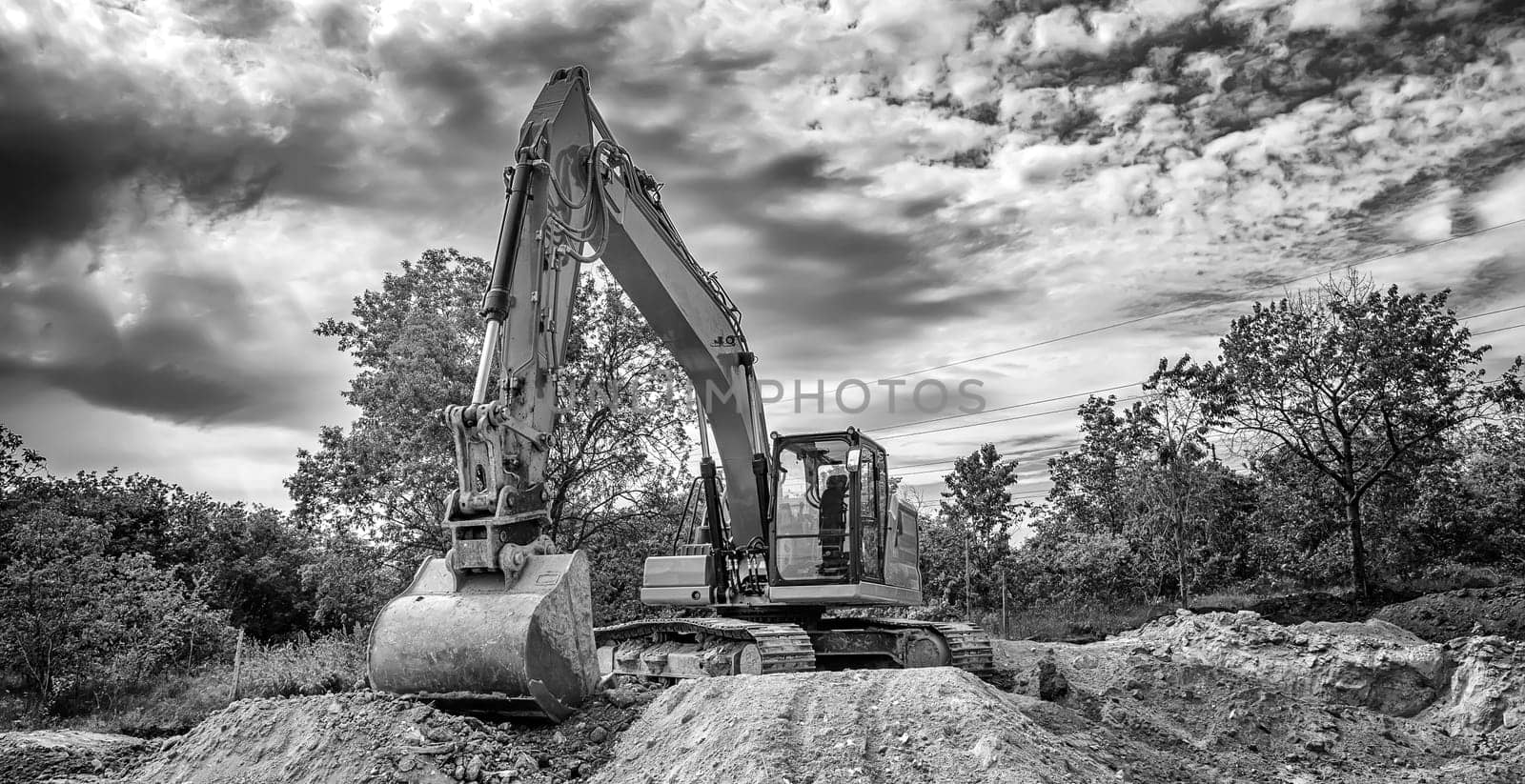 Crawler excavator during earthmoving works on construction site in black and white Banner view