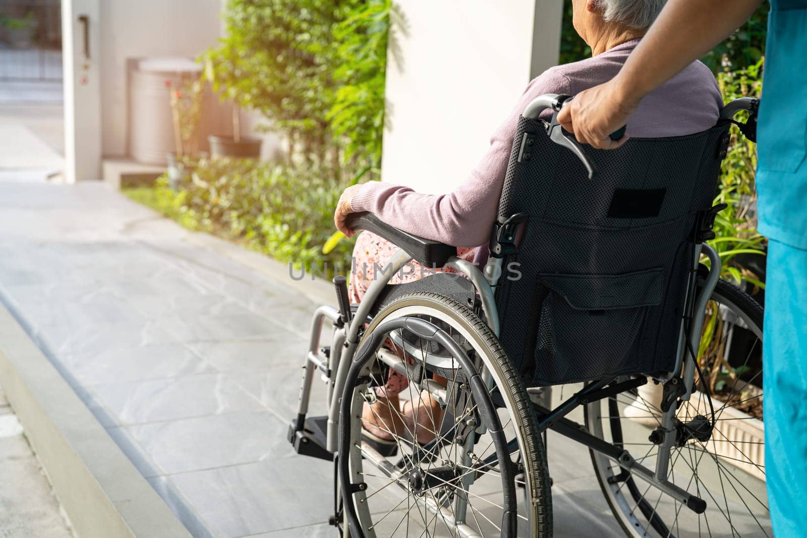 Caregiver help and care Asian elderly woman patient sitting on wheelchair to ramp in nursing hospital, healthy strong medical concept.