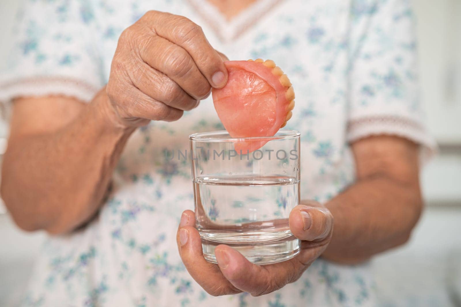 Asian senior woman patient holding and washing denture in water cleanser glass for good chewing.