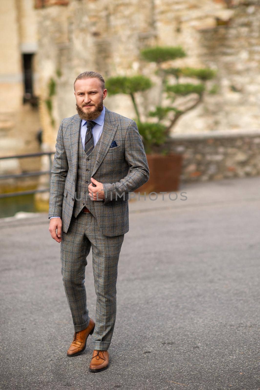 A man with a beard in a strict grey three-piece suit with a tie in the old town of Sirmione, a Stylish man in a grey suit in Italy.