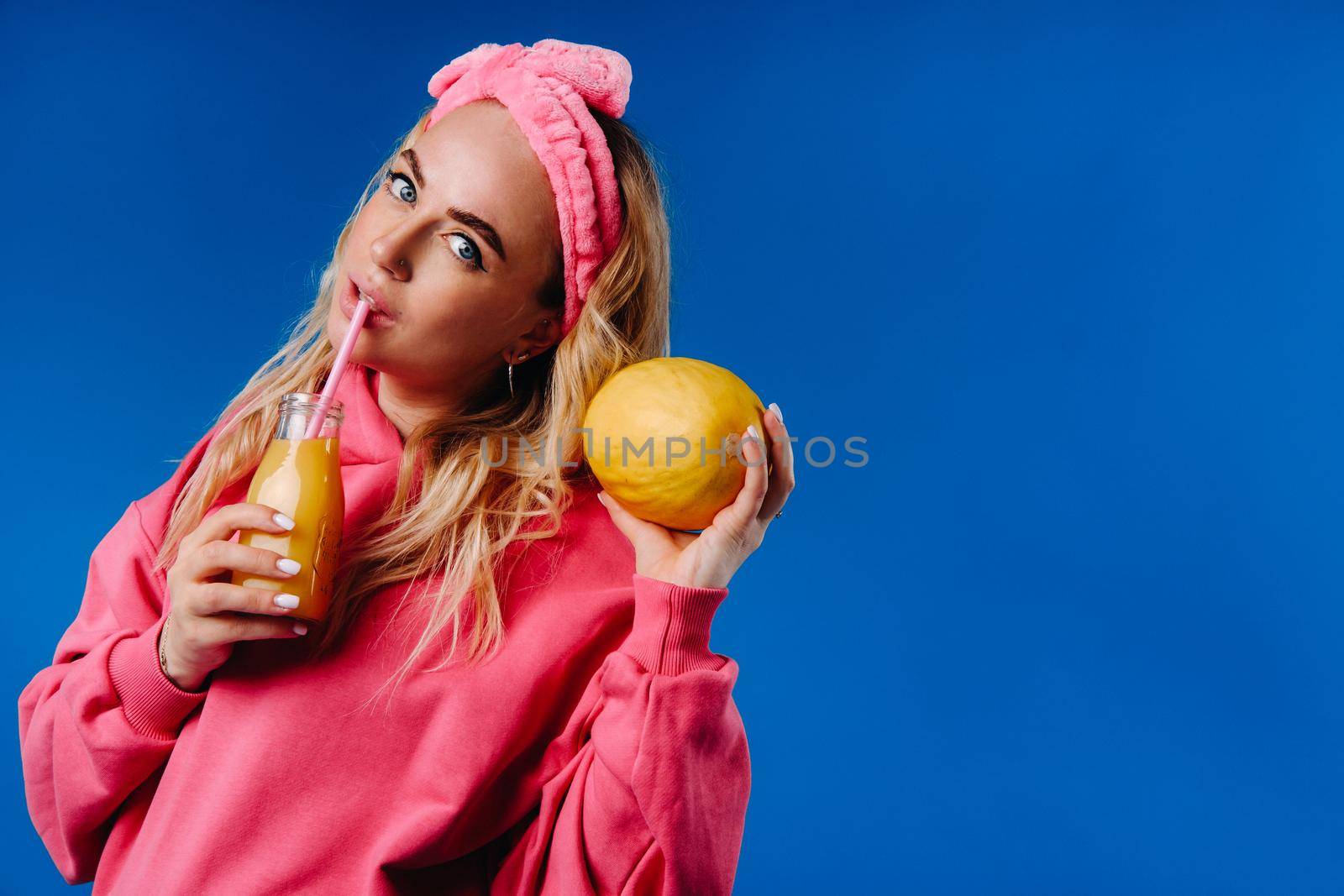 pregnant girl in pink clothes with a bottle of juice and a melon on a blue background.