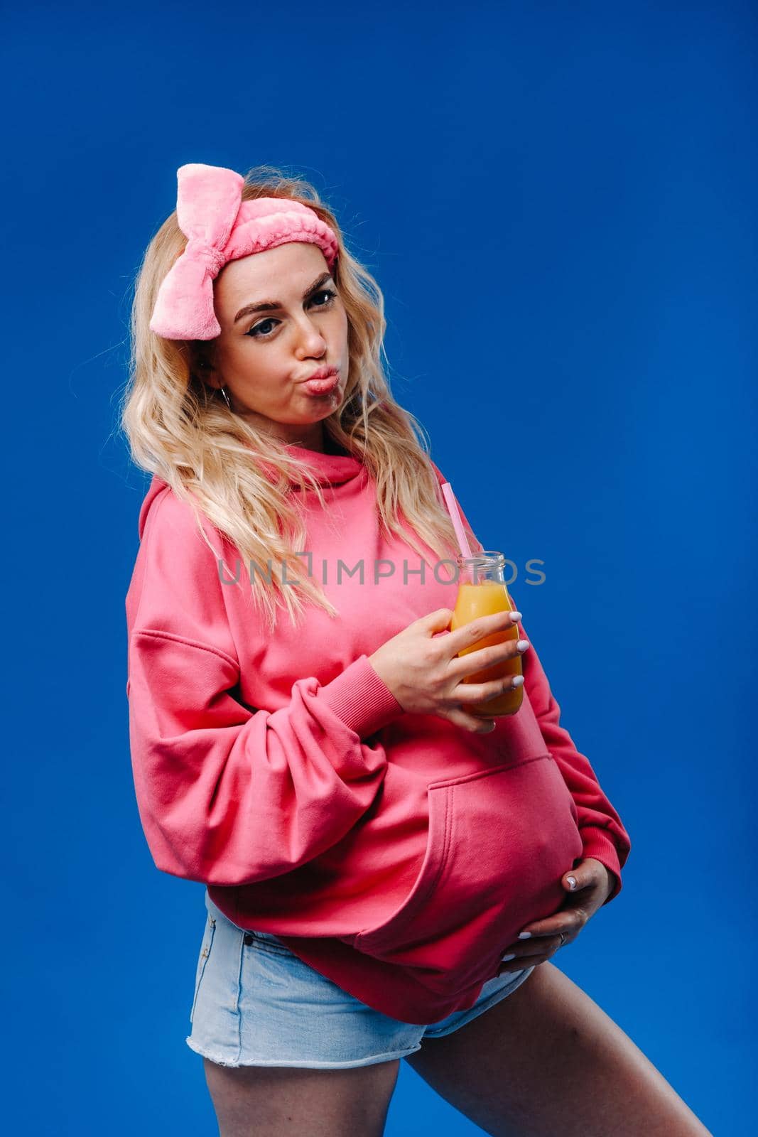 pregnant girl in pink clothes with a bottle of juice on a blue background by Lobachad