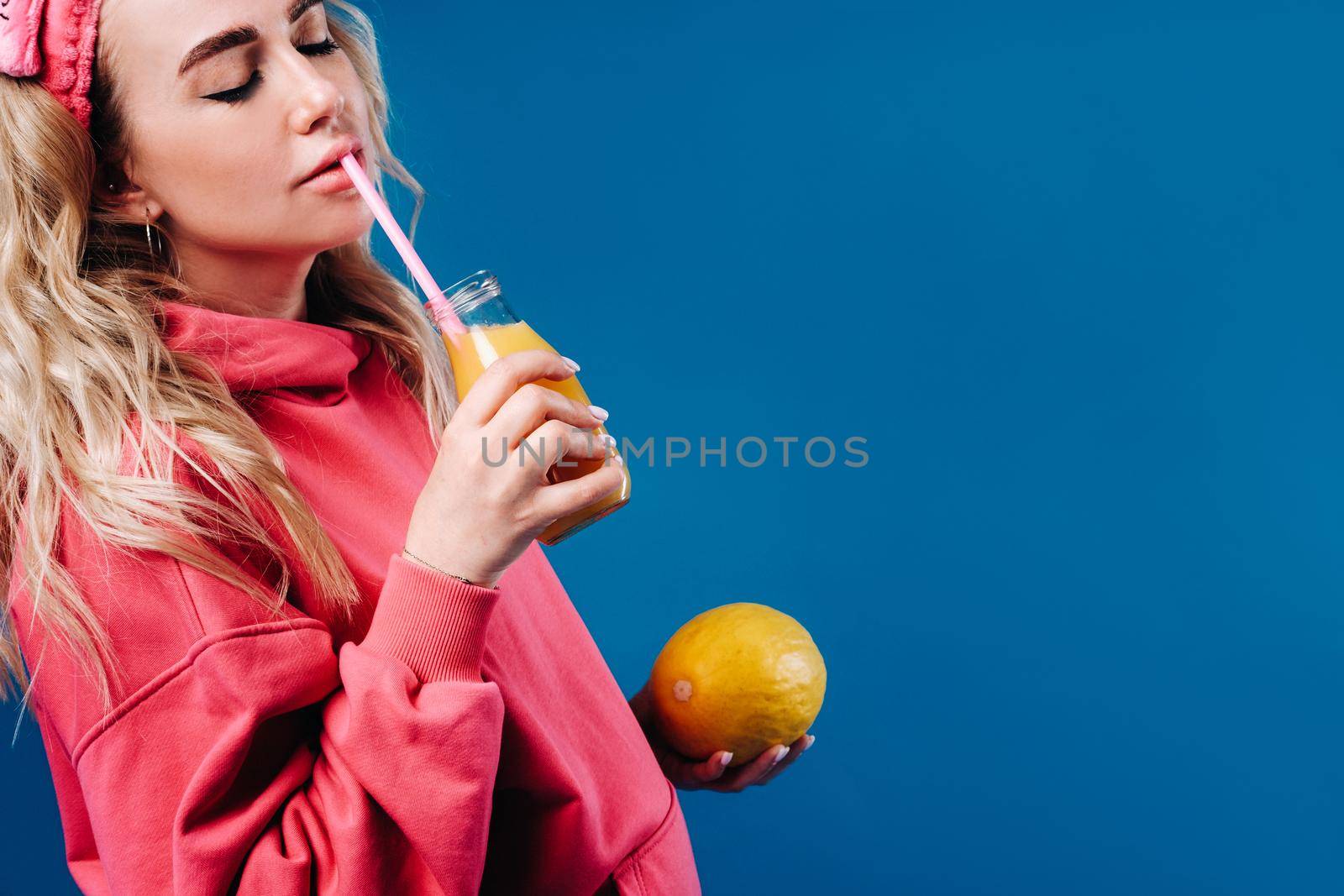 pregnant girl in pink clothes with a bottle of juice and a melon on a blue background.