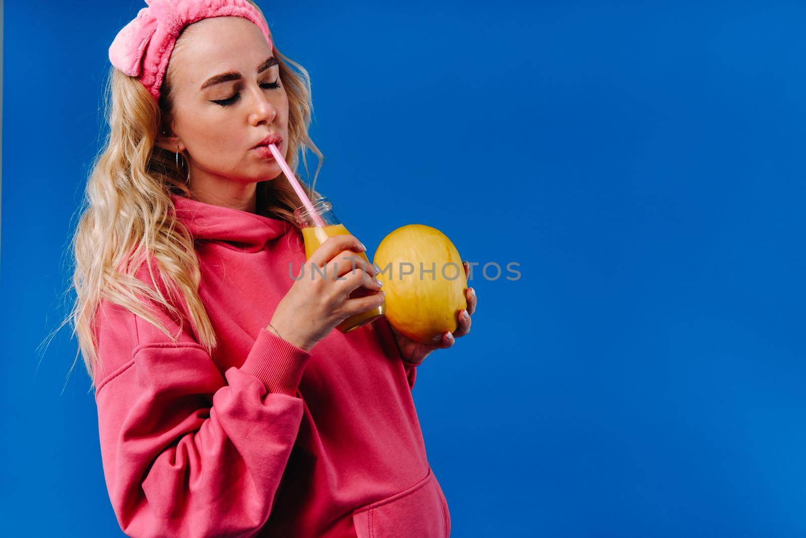 pregnant girl in pink clothes with a bottle of juice and a melon on a blue background.