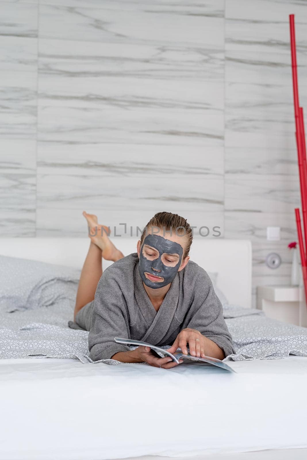 Womens health. Spa and wellness. Woman with face mask relaxing lying on the bed reading a magazine