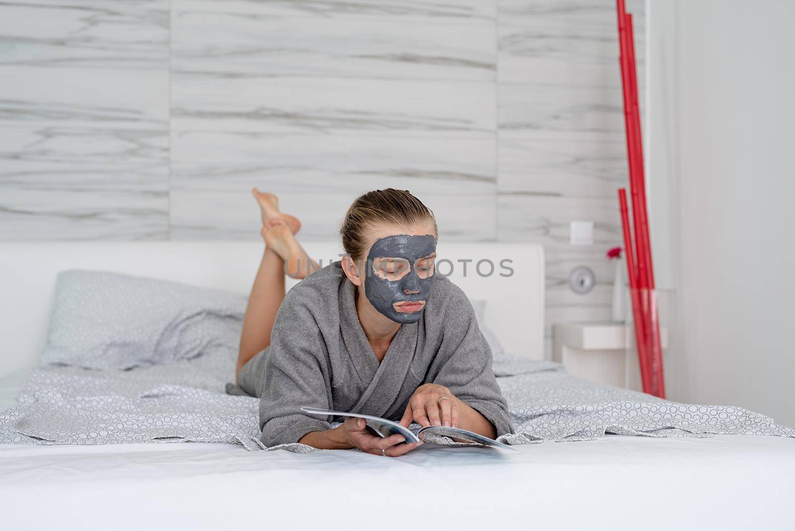 Womens health. Spa and wellness. Woman with face mask relaxing lying on the bed reading a magazine