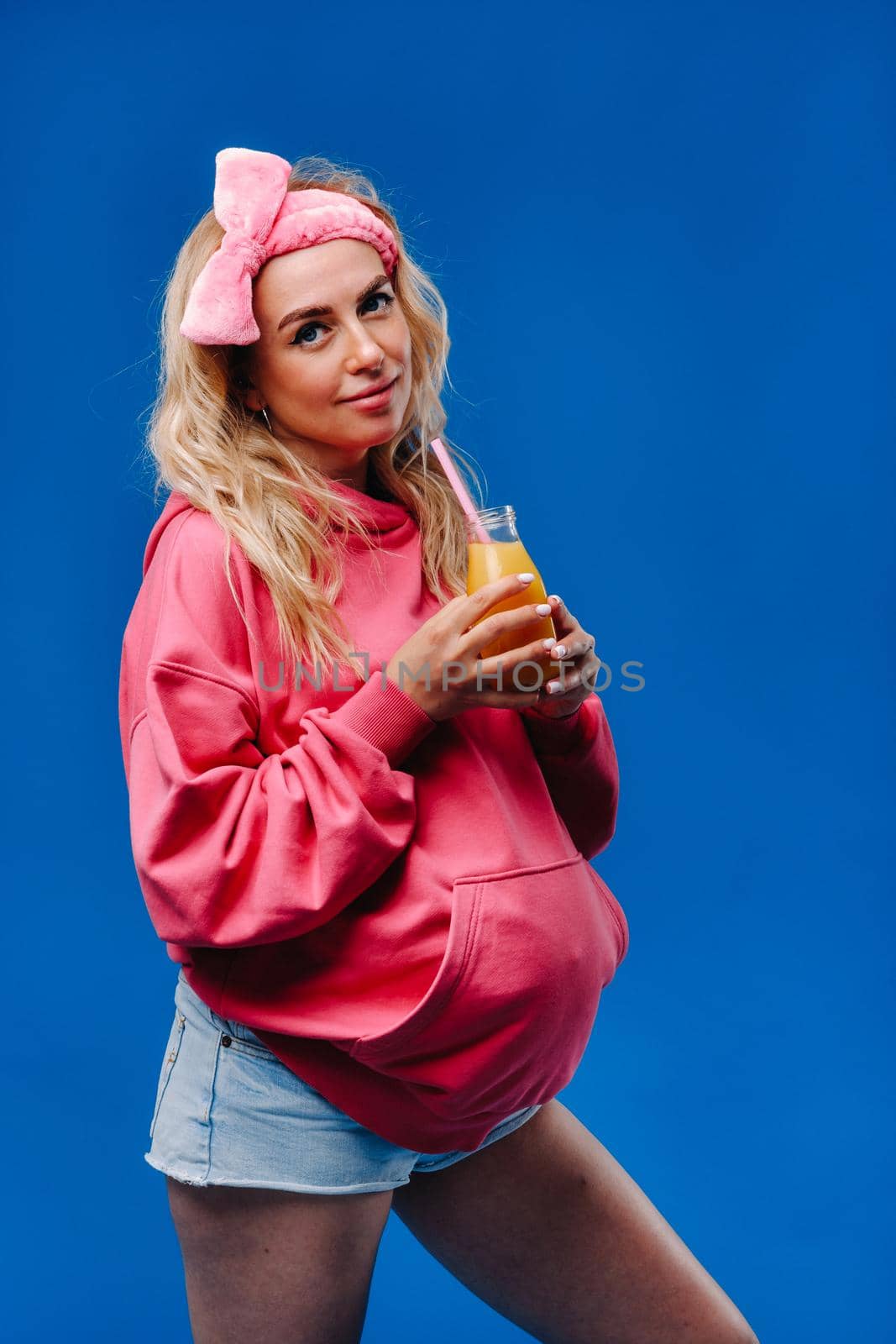 pregnant girl in pink clothes with a bottle of juice on a blue background.