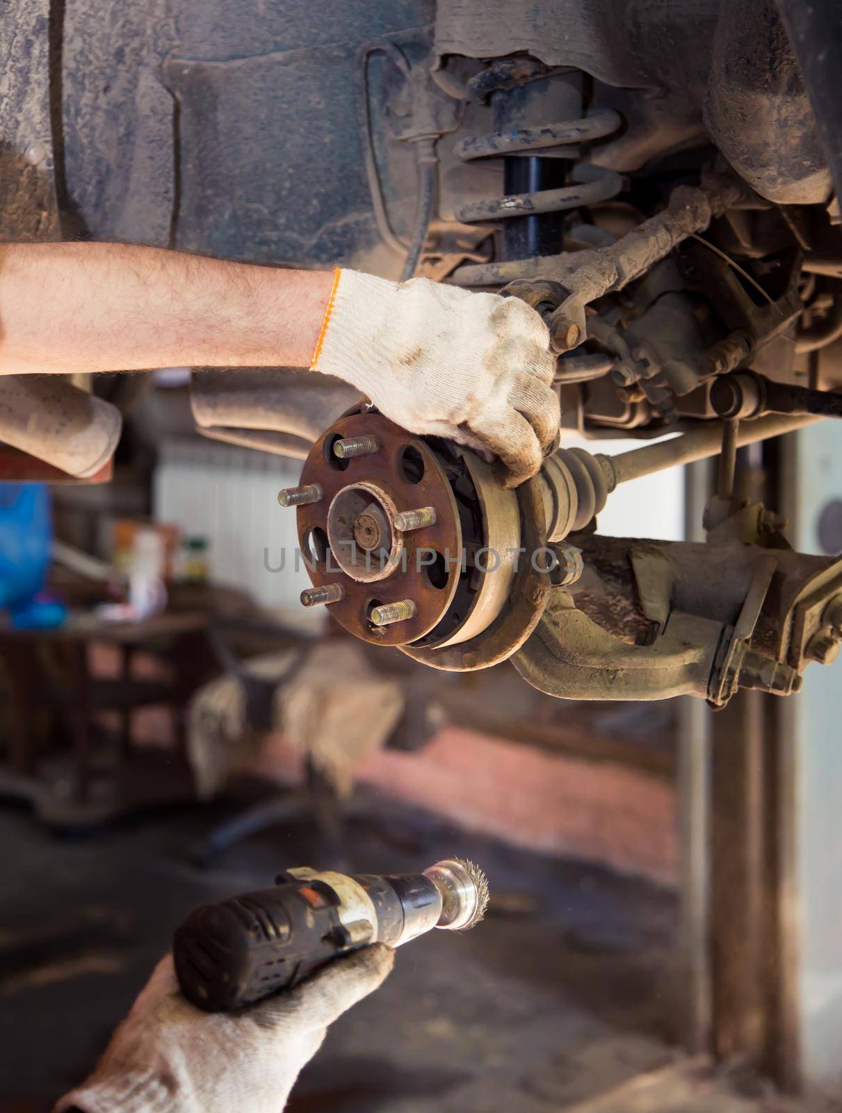 Use a power tool to remove rust from the worn rear wheel hub. In the garage, a person changes the failed parts on the vehicle. Small business concept, car repair and maintenance service.