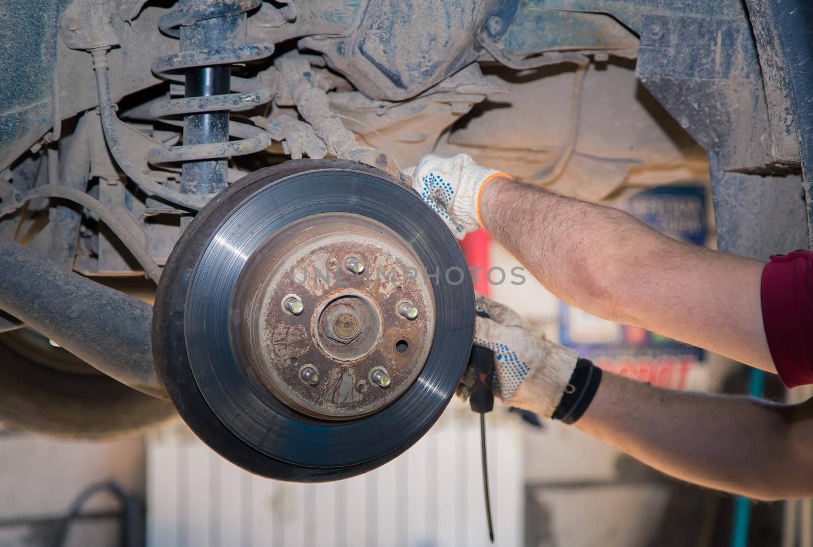 The man's hands detach the worn and rusty rear wheel disc. In the garage, a person changes the failed parts on the vehicle. Small business concept, car repair and maintenance service.