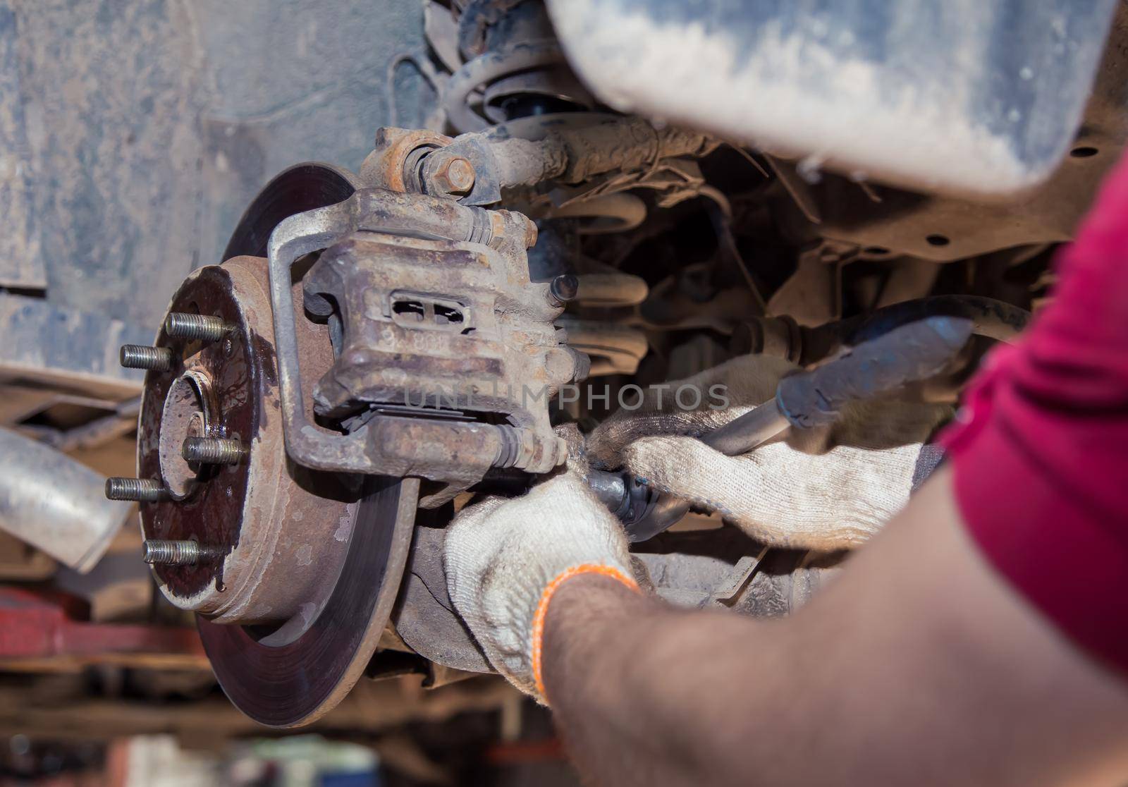 Gloved hands remove the worn rear wheel hub support. In the garage, a person changes the failed parts on the vehicle. Small business concept, car repair and maintenance service.