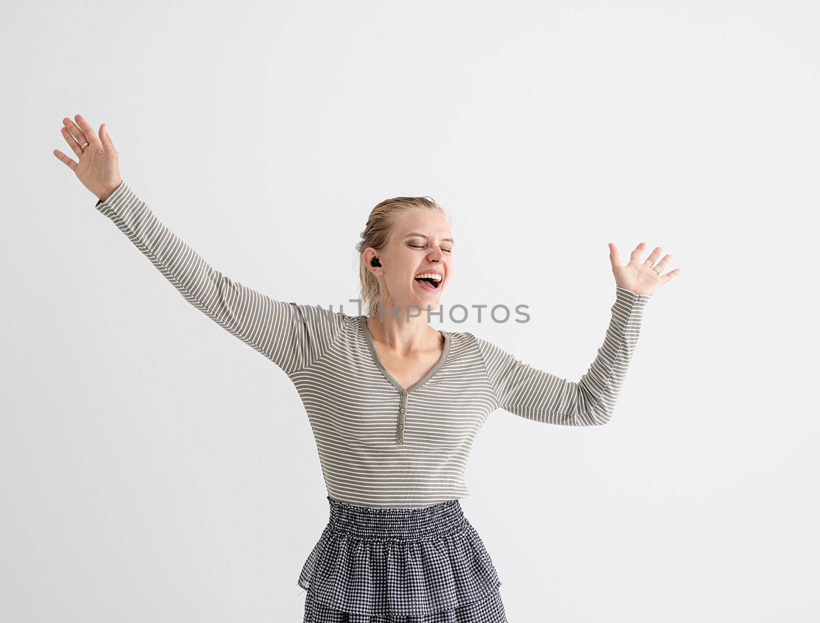 Young woman holding wireless earbuds and dancing by Desperada