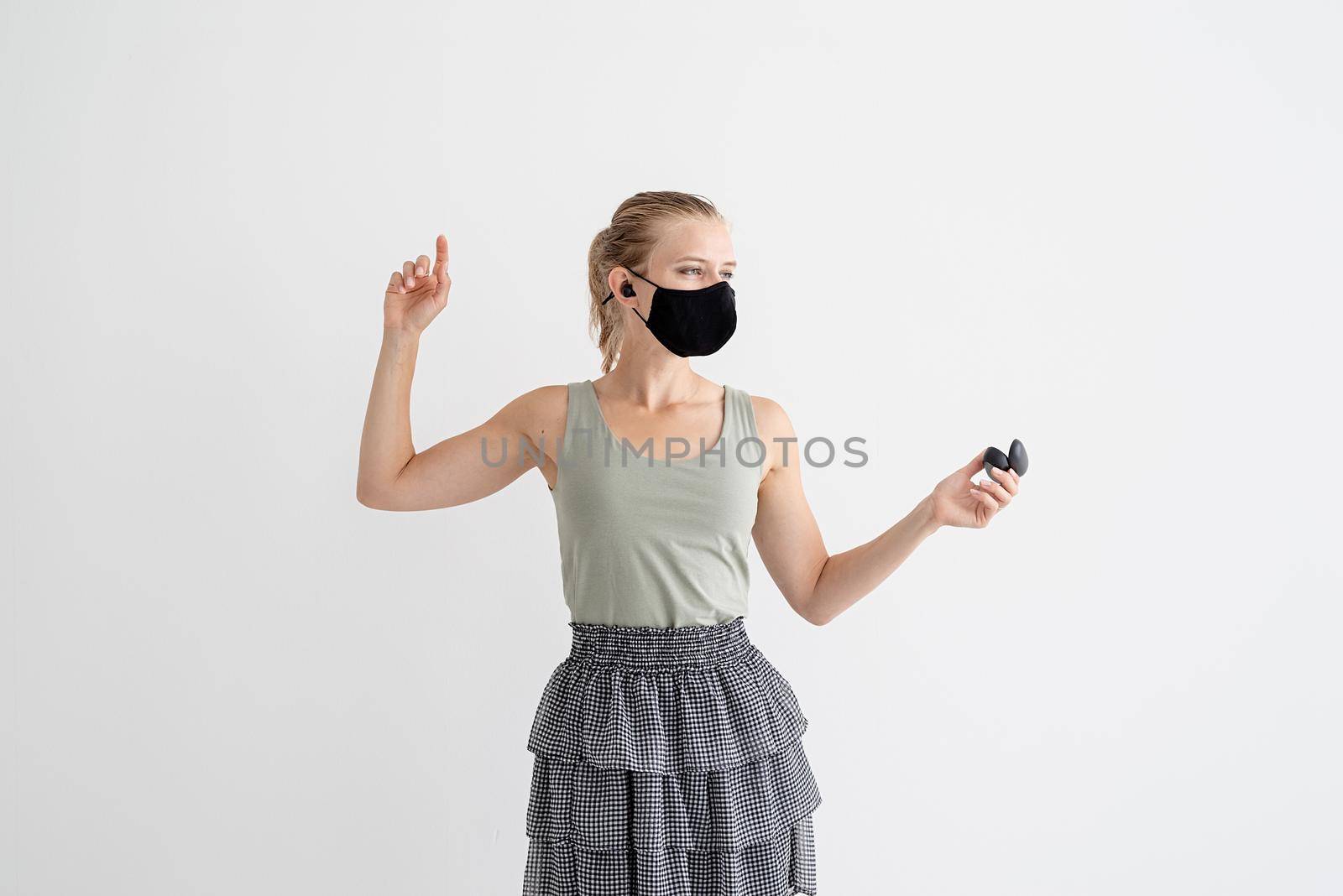 Music, isolation and leisure. Young woman in a protective mask holding wireless earbuds and dancing