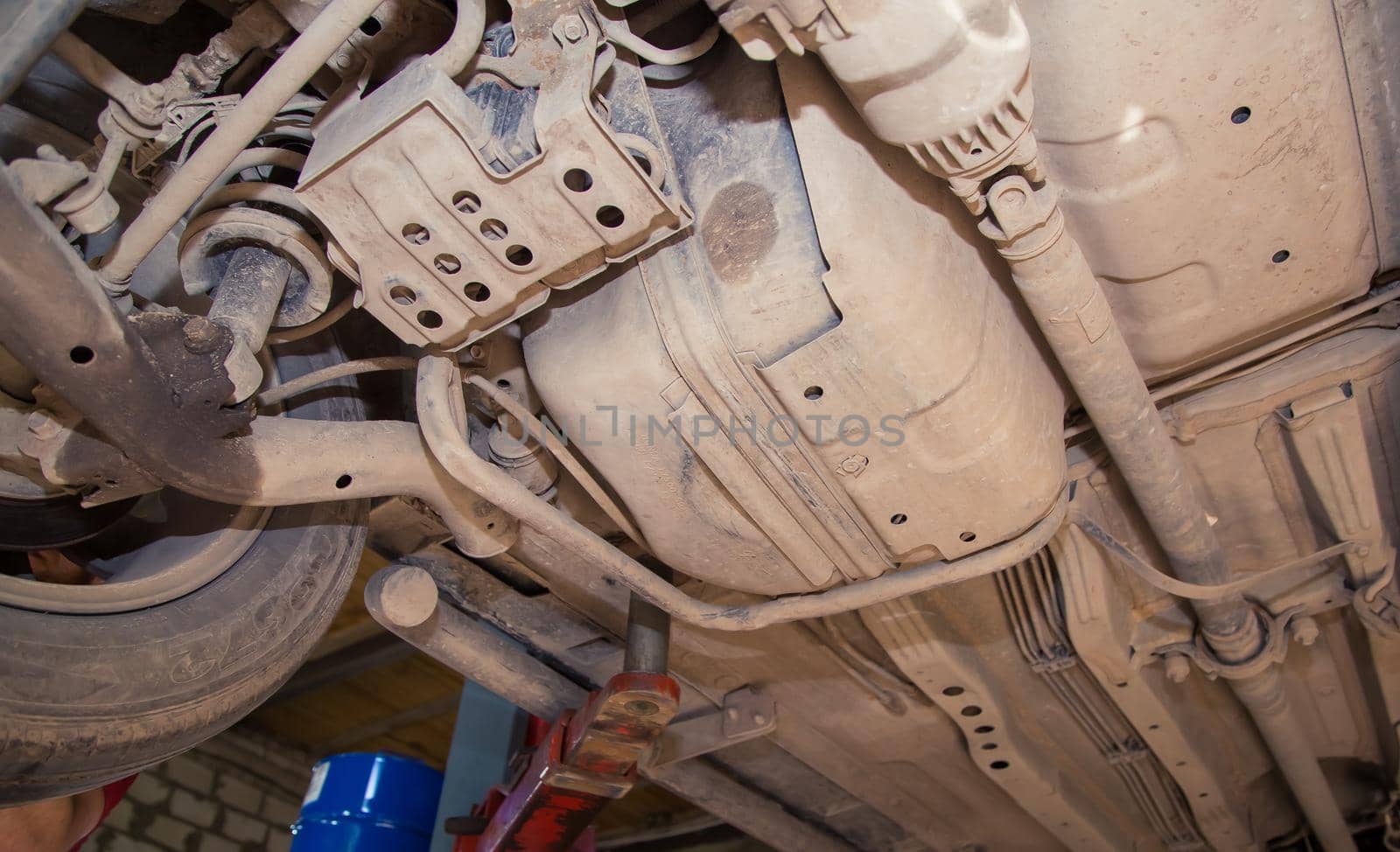 Bottom view of the raised car, gas tank, transfer shaft, rear wheel. In the garage, a person changes the failed parts on the vehicle. Small business concept, car repair and maintenance service.