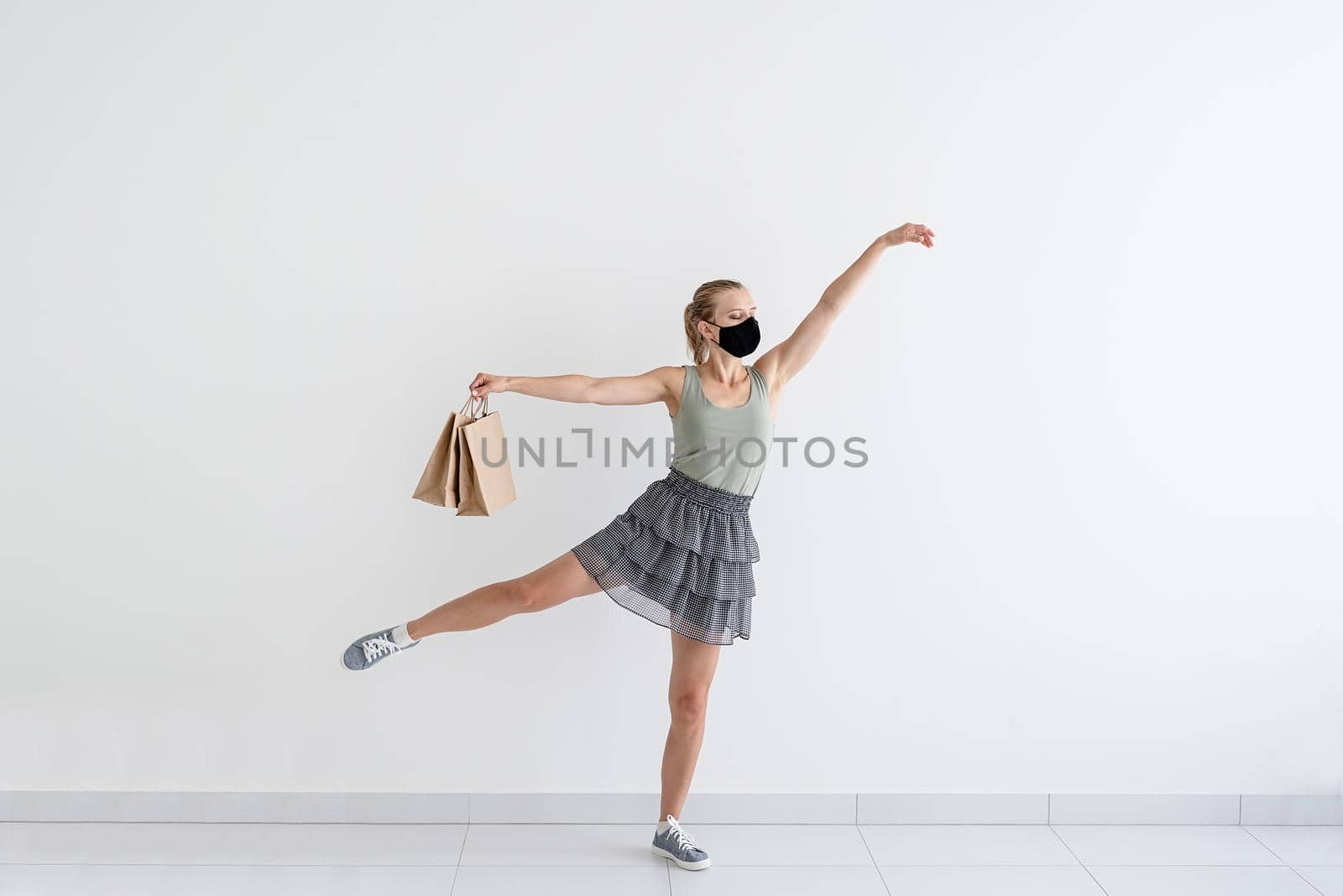 Young woman dancing ballet with shopping bags in a protective mask by Desperada