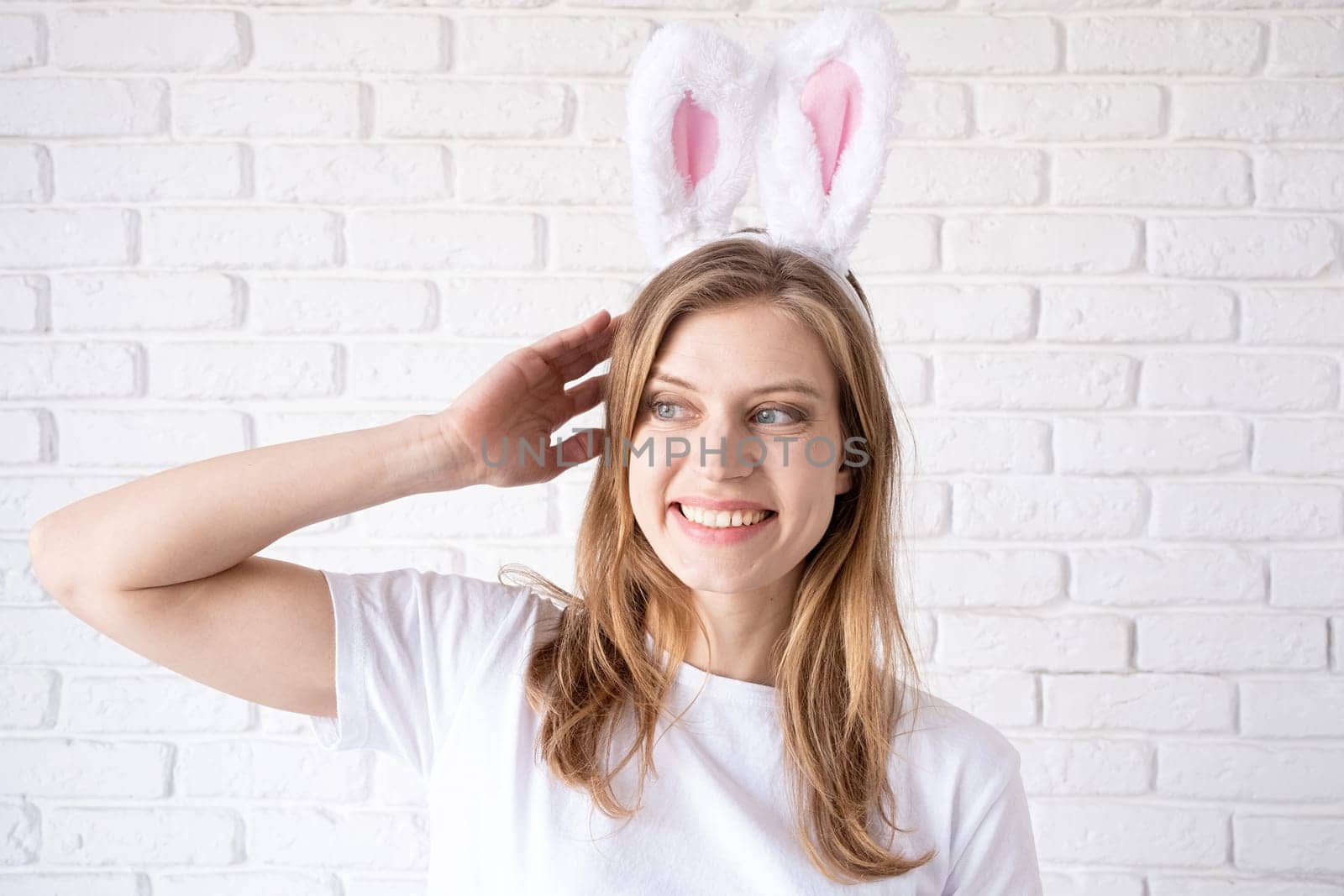 Spring holidays, Easter. Portrait of a happy woman in bunny ears on white brick wall background