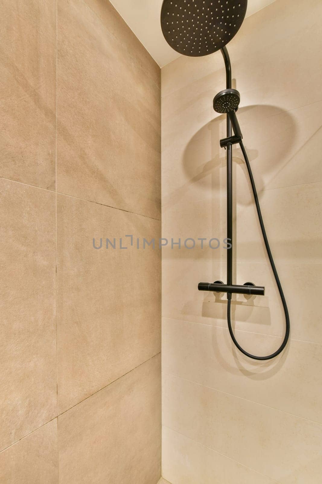 a shower that is in the corner of a room with beige tiles on the walls, and a black hand held shower head