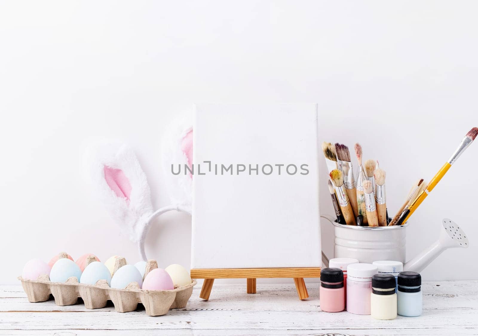 Spring holidays, Happpy Easter. Pastel colored Easter eggs and mimosa flowers with blank white frame for mockup design, front view on white brick wall background