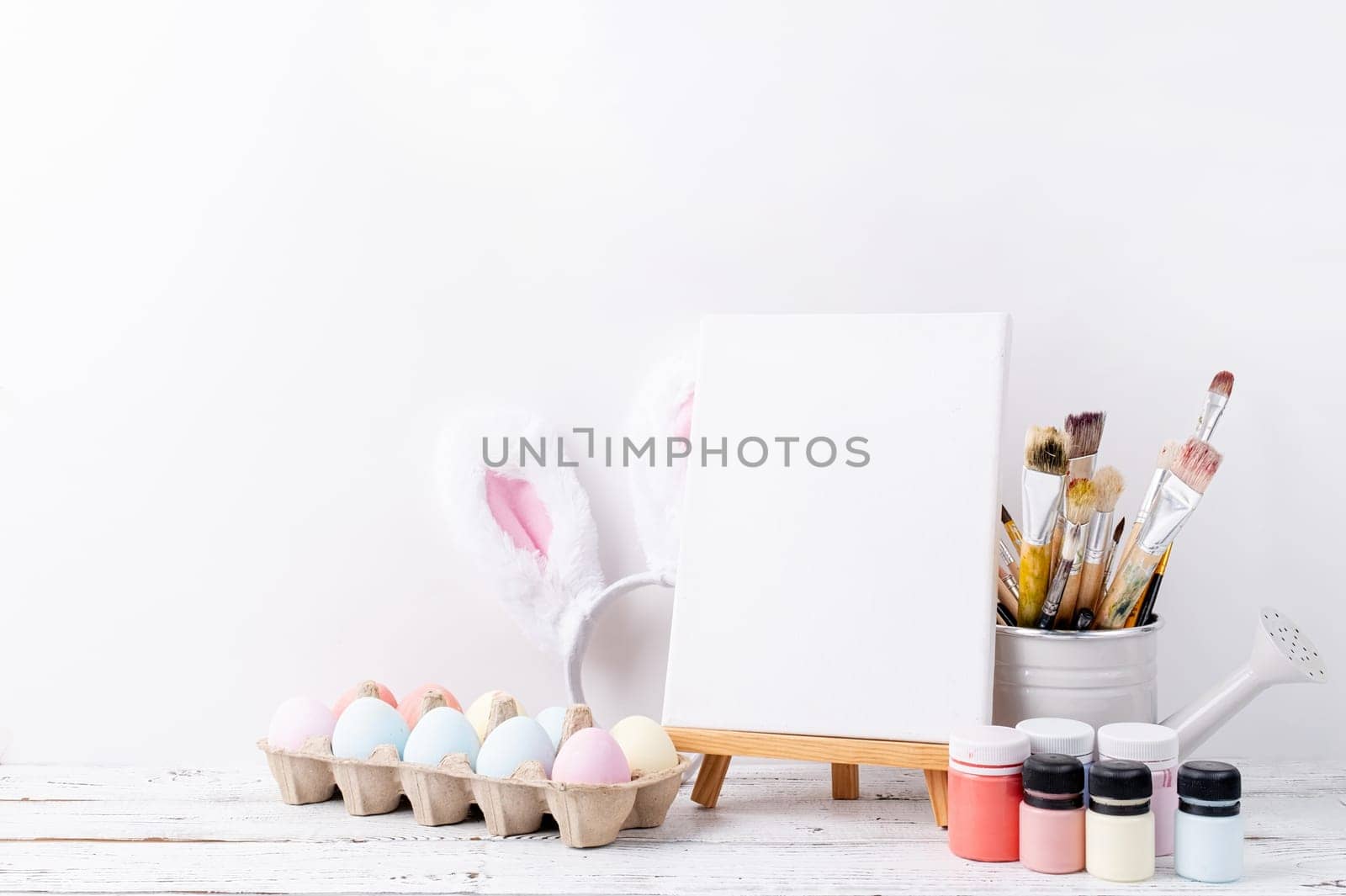 Spring holidays, Happpy Easter. Pastel colored Easter eggs and mimosa flowers with blank white frame for mockup design, front view on white brick wall background