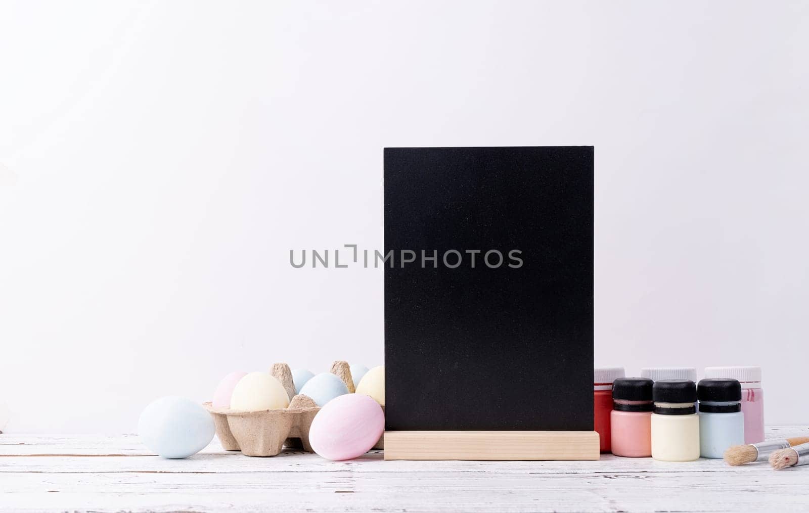 Spring holidays, Happpy Easter. Pastel colored Easter eggs and mimosa flowers with blank white frame for mockup design, front view on white brick wall background