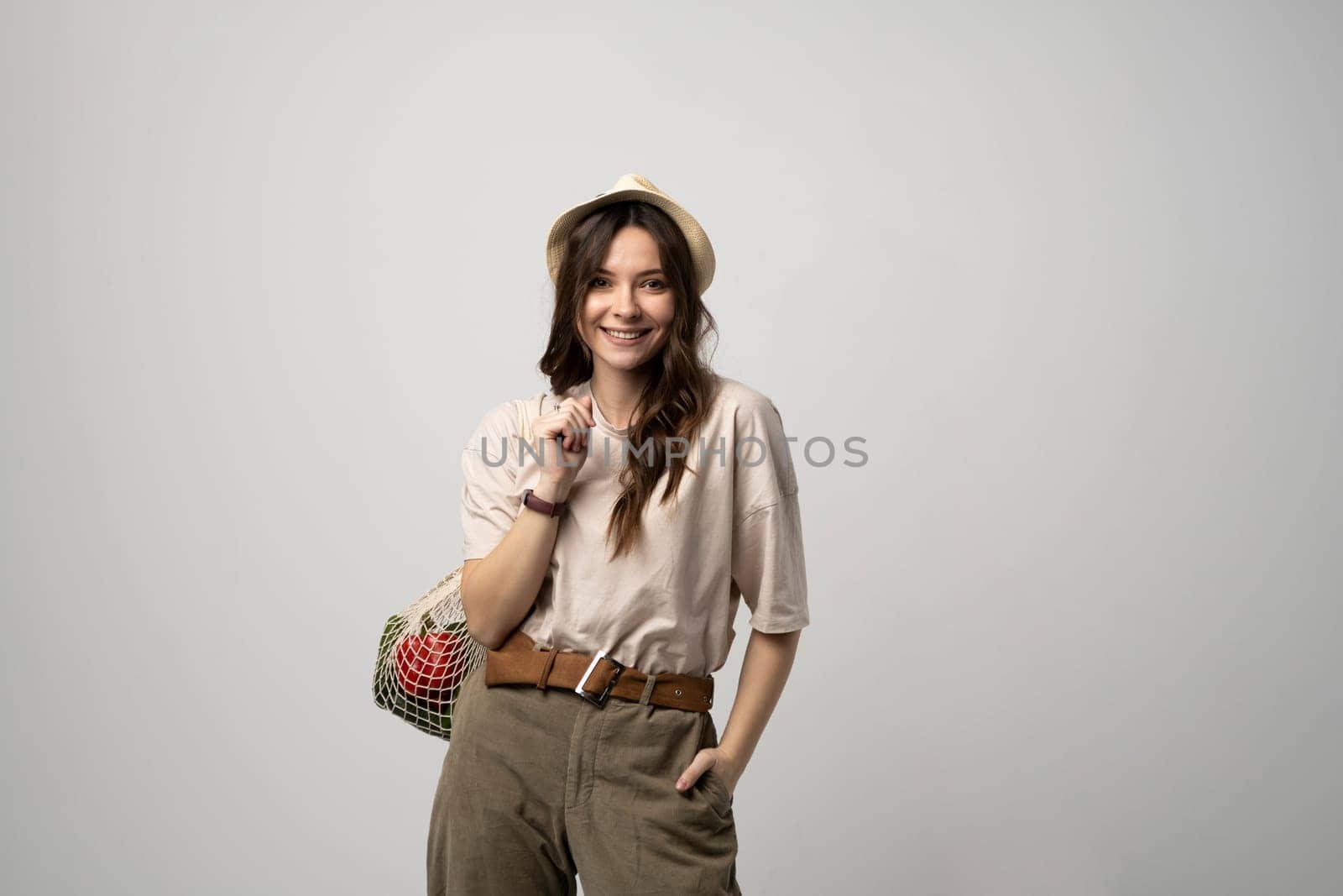 Woman in a beige t-shirt and a hat holding mesh shopping bag with groceries. Conscious consumption. Eco trend. Zero waste concept. Girl carry bag shopper