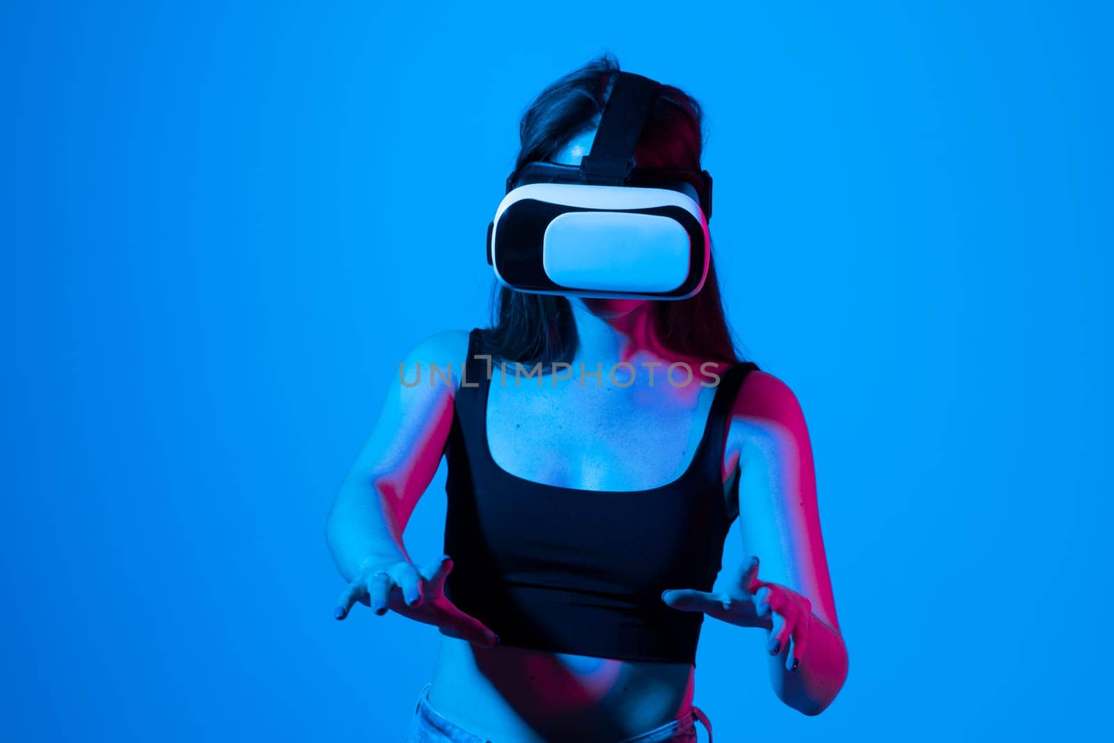 Young woman wearing virtual reality goggles and speasing with a friends in the metaverse. Famale in a black top exploring virtual reality video games in a studio. by vovsht