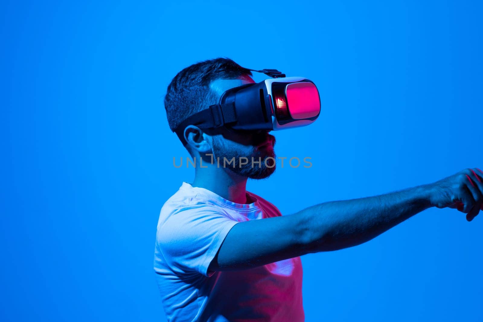 Bearded brunette male in vr glasses plays online, work or study with technology of future, explores virtual world, in neon light. Entertainment and game with modern gadget and 3D simulation