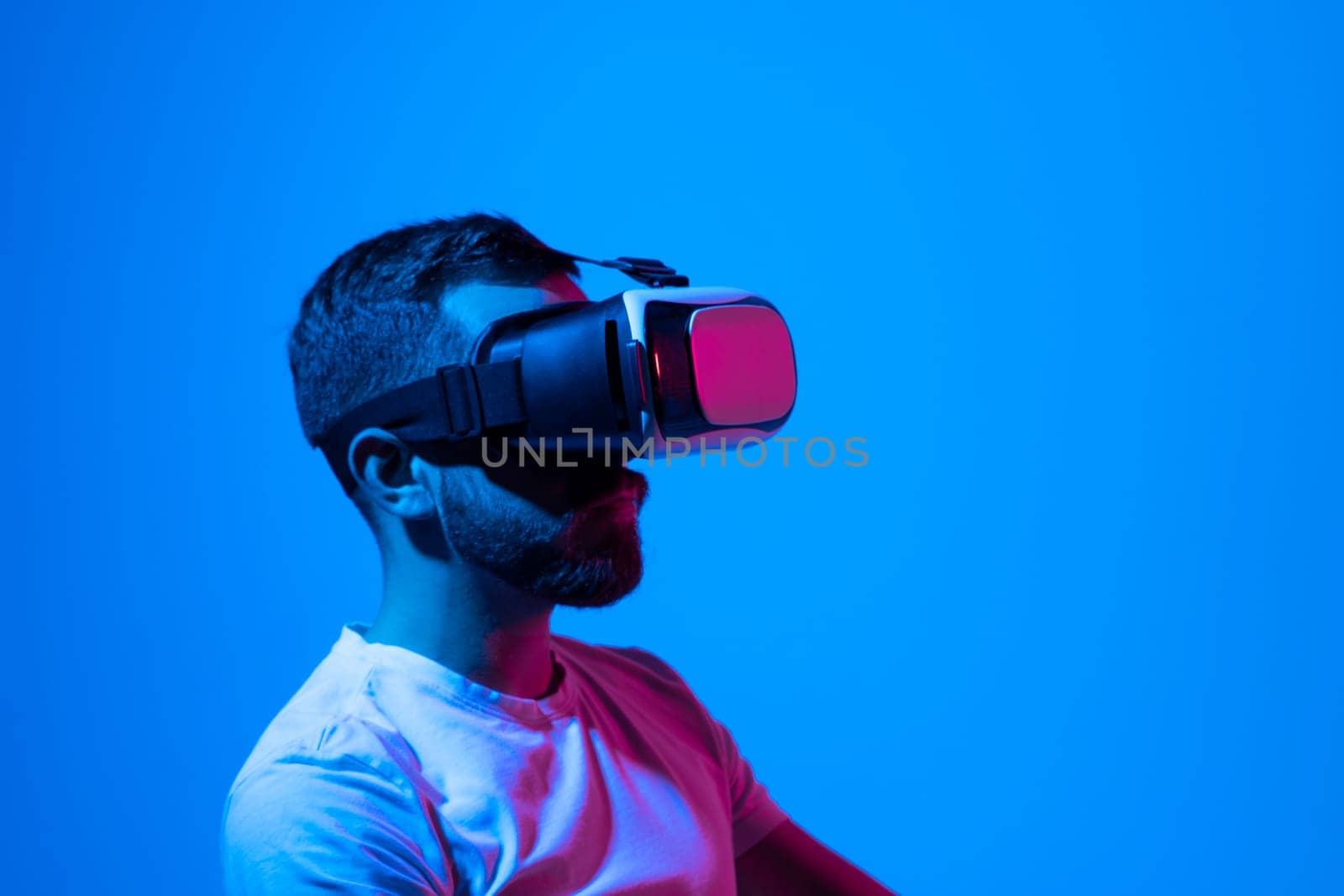 Bearded man in white t-shirt wearing Virtual Reality VR Headset ang playing a game online. VR for gaming. Man play game in VR glasses